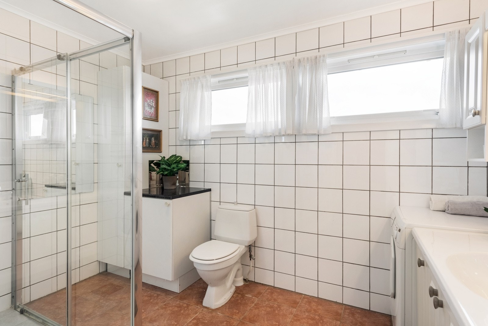 Badet har god størrelse, og jordfargede gulvfliser kombineres med hvite fliser på veggene. Galleribilde