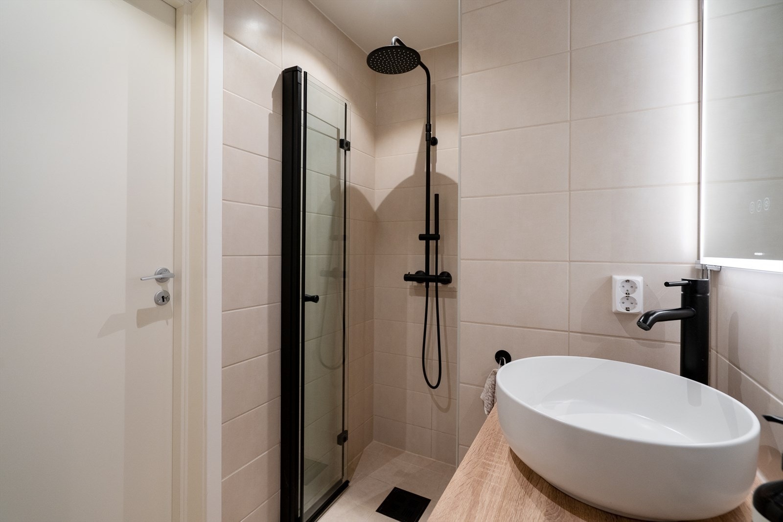 Badet er utstyrt med et veggmontert toalett, servantinnredning, dusjnisje med glassdør og opplegg for toppmatet vaskemaskin. Galleribilde