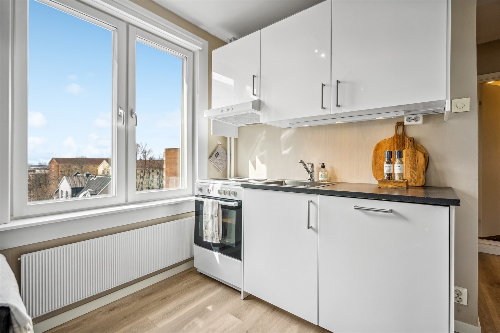 Kjøkkeninnredningen består bl.a. av glatte fronter, laminat benkeplate med nedfelt kum i rustfritt stål og integrert oppvaskmaskin. Galleribilde