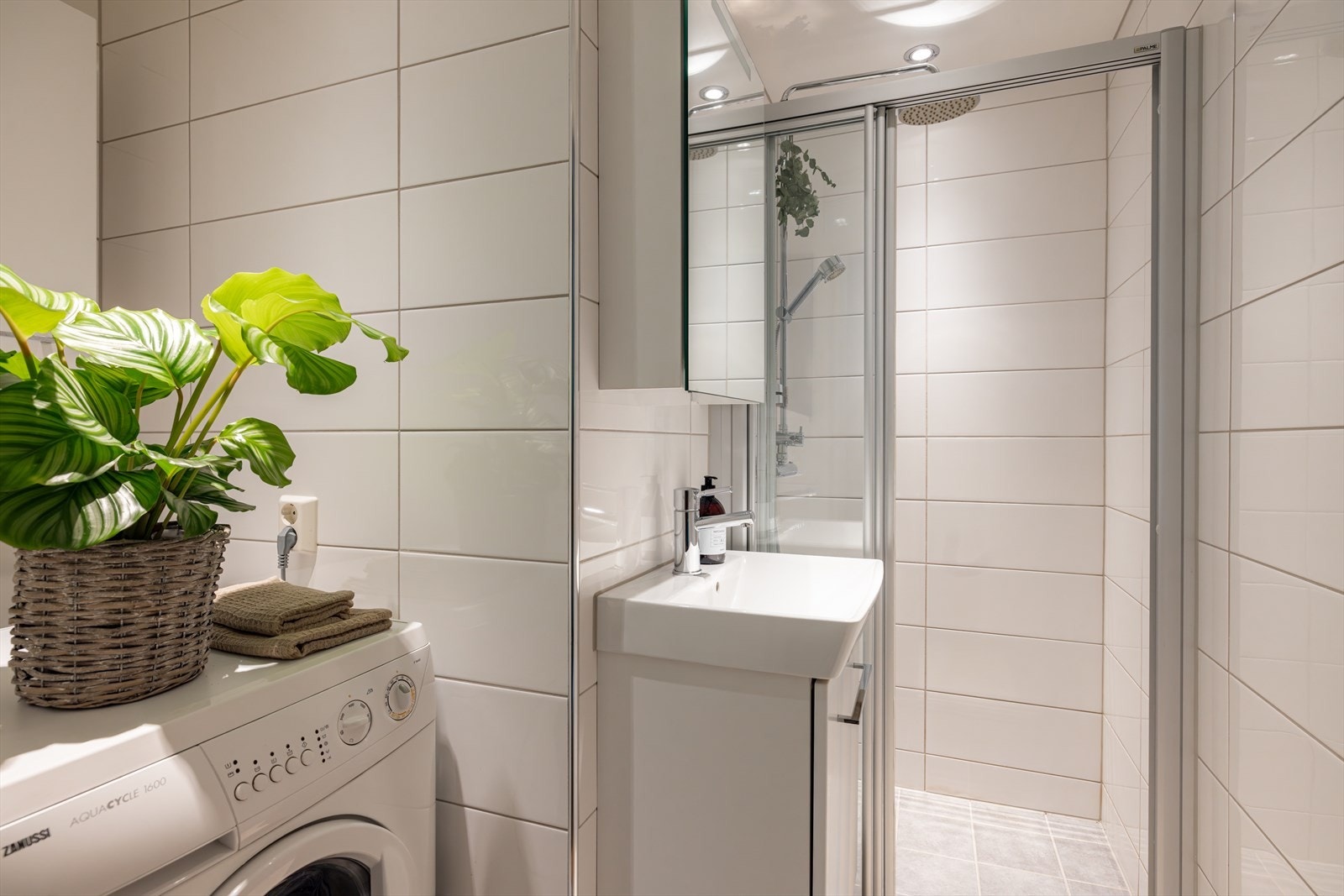 Det lyse, flislagte badet er innredet med dusj, vask og opplegg for vaskemaskin. Galleribilde