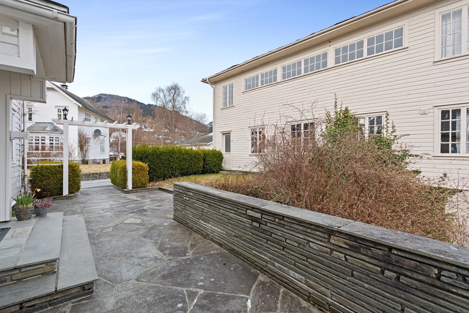 Pent opparbeida inngangsparti med hellelagt tilkomst, murar og beplantning. Galleribilde