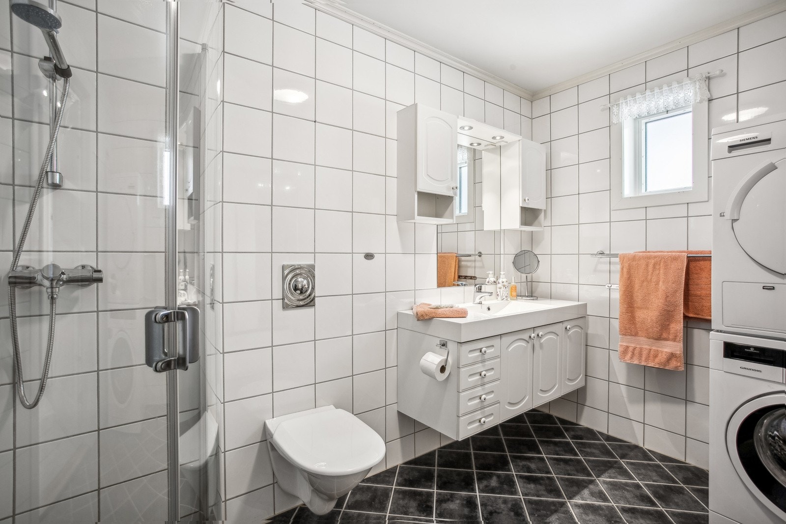 Baderommet har lys innredning med servant, speil, veggmontert toalett, dusjhjørne med glassvegger og opplegg for vaskemaskin og tørketrommel. Galleribilde