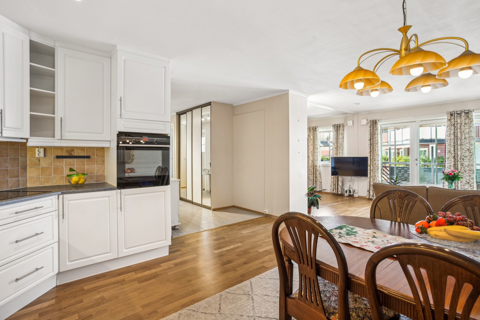 Lys kjøkkeninnredning med profilerte fronter, benkeplater i laminat, fliser mellom benkeplater og overskap, dobbel oppvaskkum med ett-greps blandebatteri og ventilator over kokesonen. Galleribilde