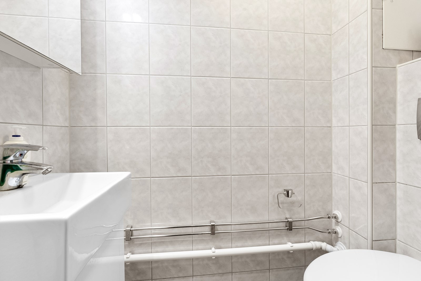 Pent flislagt wc rom med innredning bestående av klosett og servantinnredning med speilskap Galleribilde