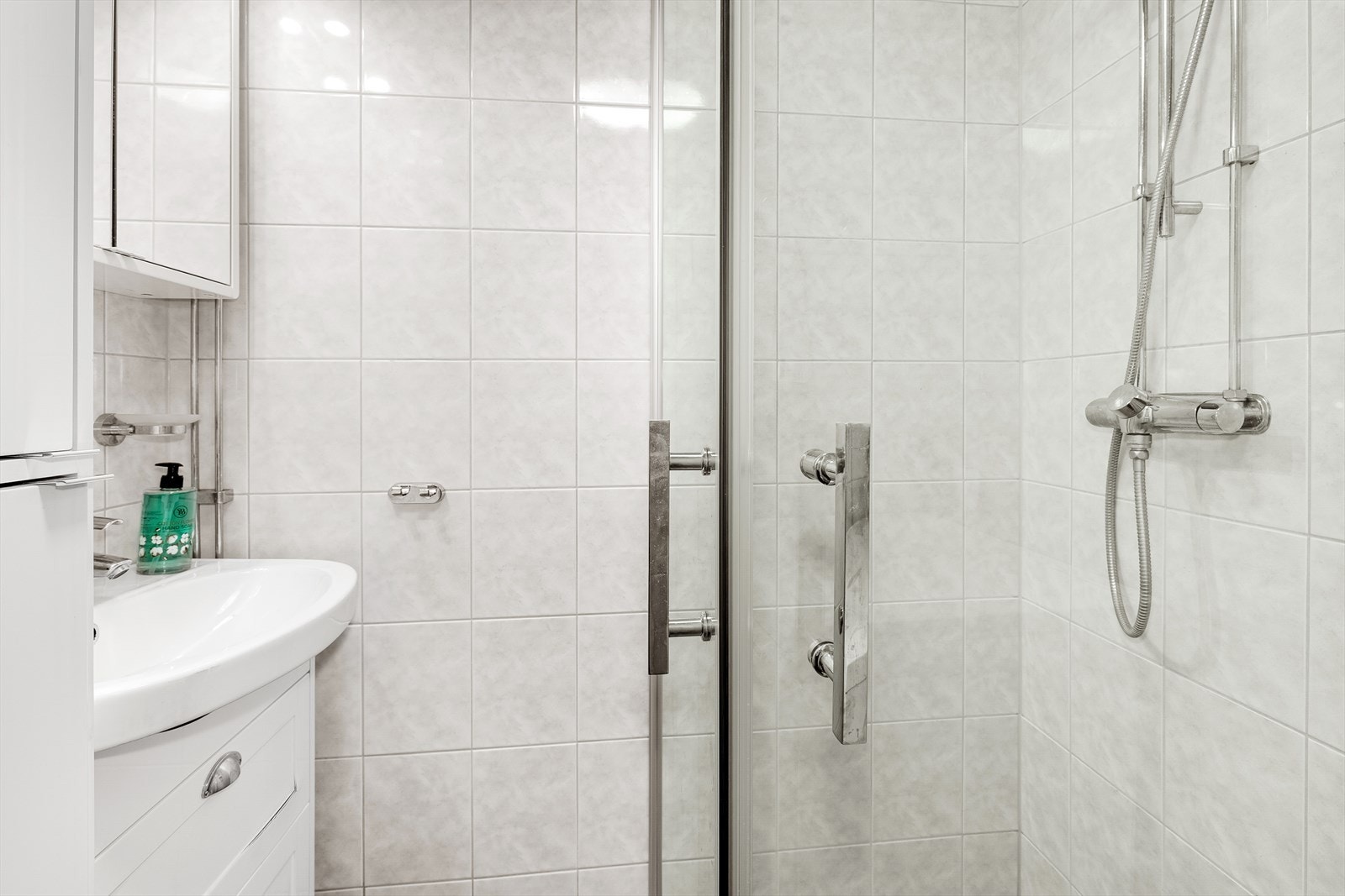 Pent flislagt bad med varmekabler i gulv. Innredning er bestående av dusjhjørne med innfellbare dører og servantinnredning med speilskap Galleribilde