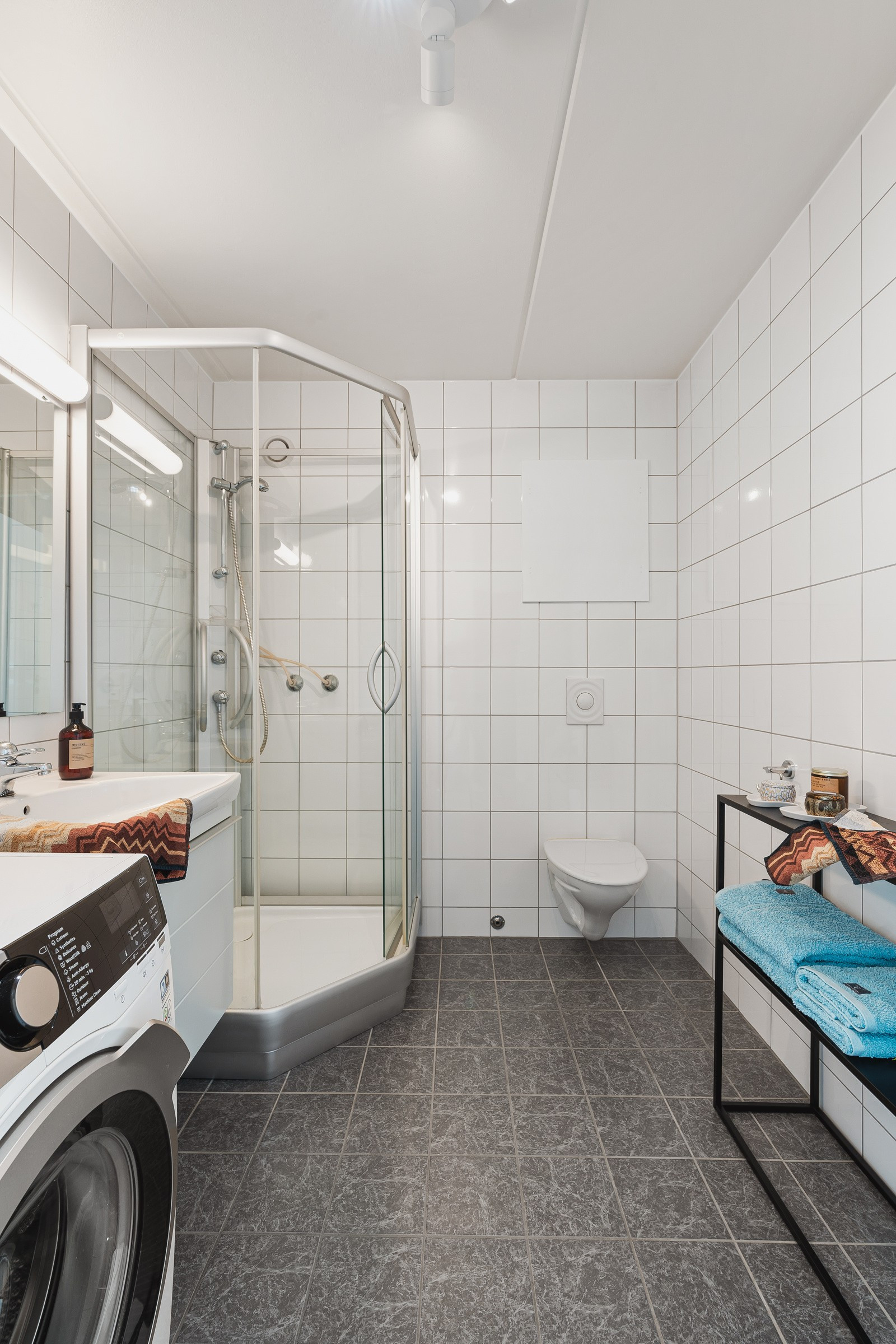 Det flislagte badet er utstyrt med praktisk vegghengt toalett, dusjkabinett og baderomsinnredning med oppbevaringsplass.
