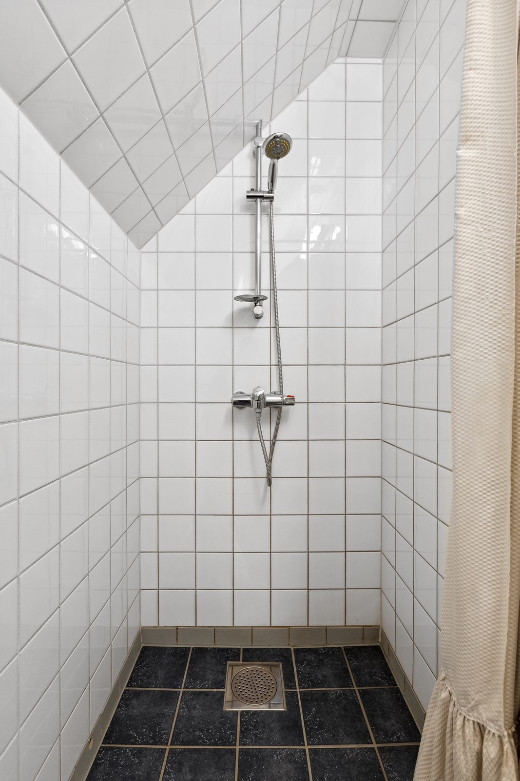Badet har en åpen dussjsone med dusjgarnityr på vegg. Galleribilde