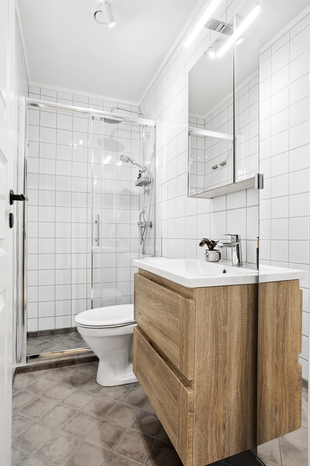 Flislagt bad med varmekabler i gulv. Badet er innredet med dusjnisje, veggmontert servant- og speilskap, samt gulvstående klosett. Galleribilde