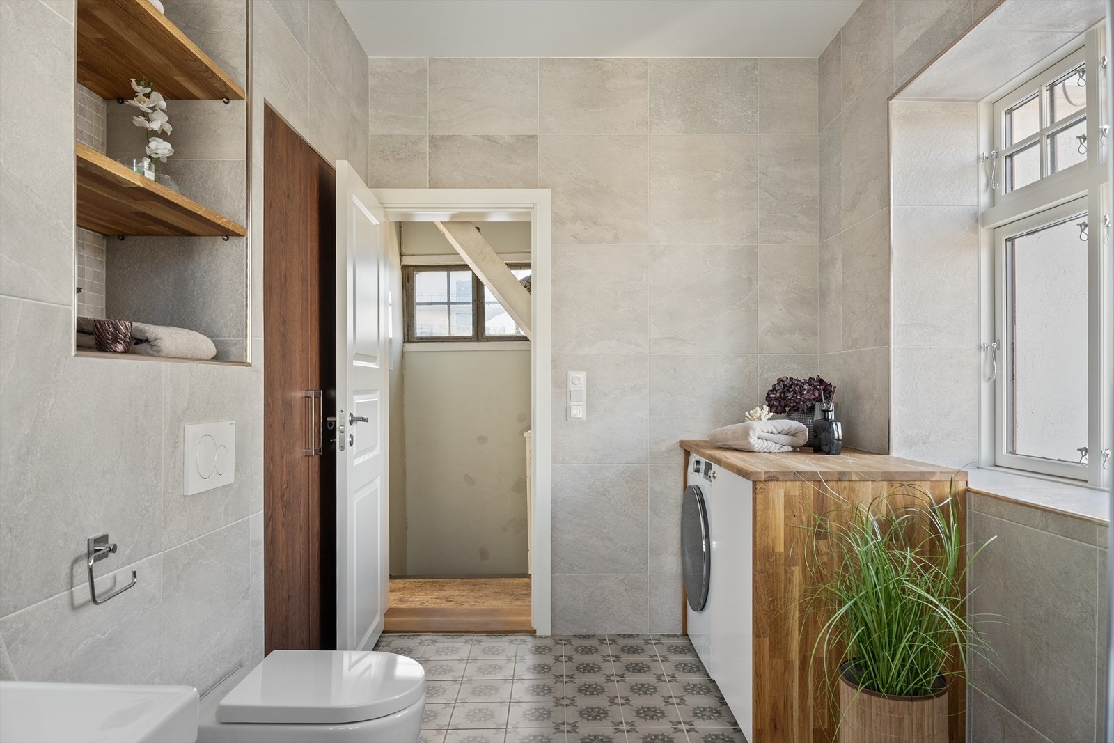 Badet er innredet med veggmonterte dusjvegger, termostat batteri, veggmontert klosett, servant med skuffer og speil med belysning. Galleribilde