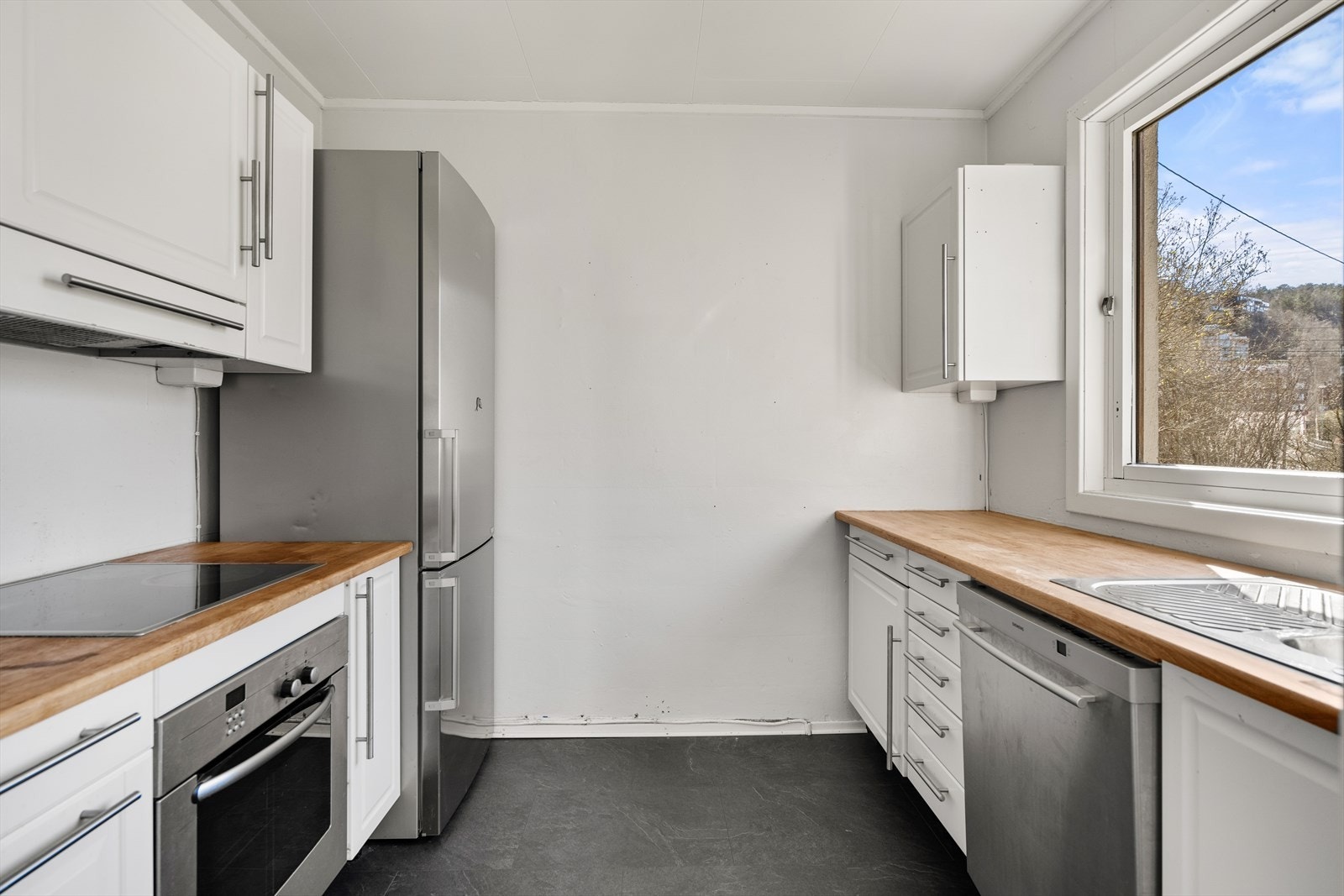 Kjøkkeninnredning med hvite profilerte fronter, benkeplater i heltre, rustfri oppvaskkum med avrenningsplate, ventilator, opplegg for oppvaskmaskin og integrerte hvitevarer. Galleribilde