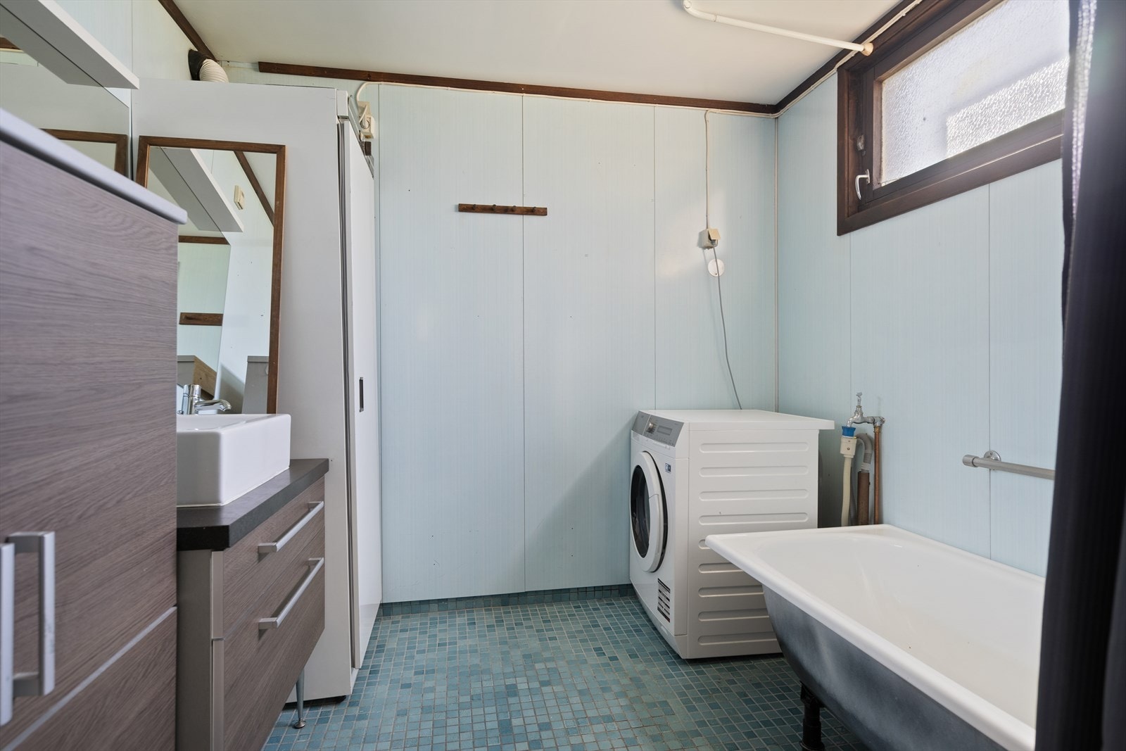 Bad med badekar, servant med skuffer, speil og plass for vaskemaskin. Galleribilde