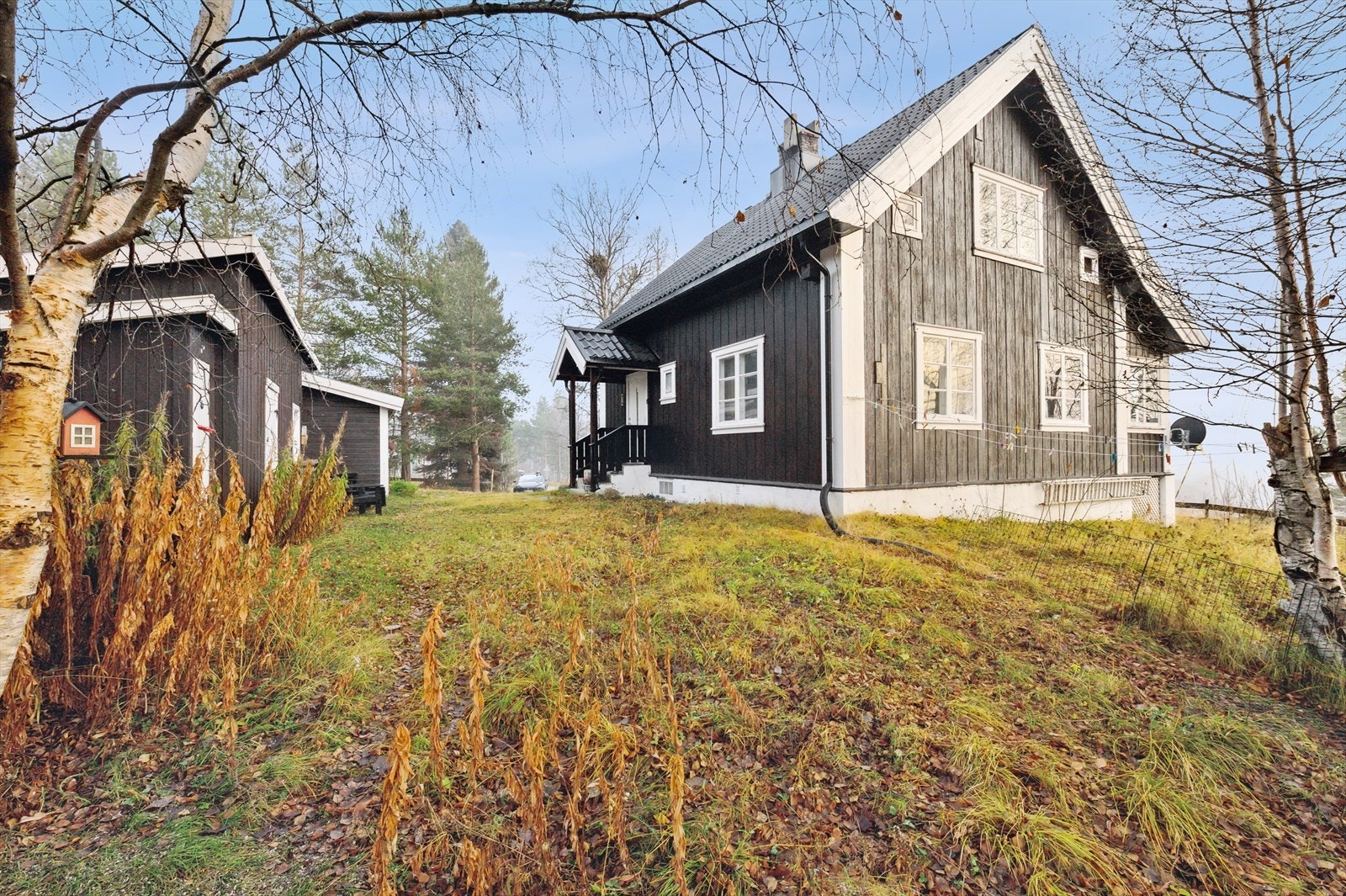 Inngjerdet tomt som er pent opparbeidet med gressbevokste områder, trær, busker og blomsterbed. Galleribilde