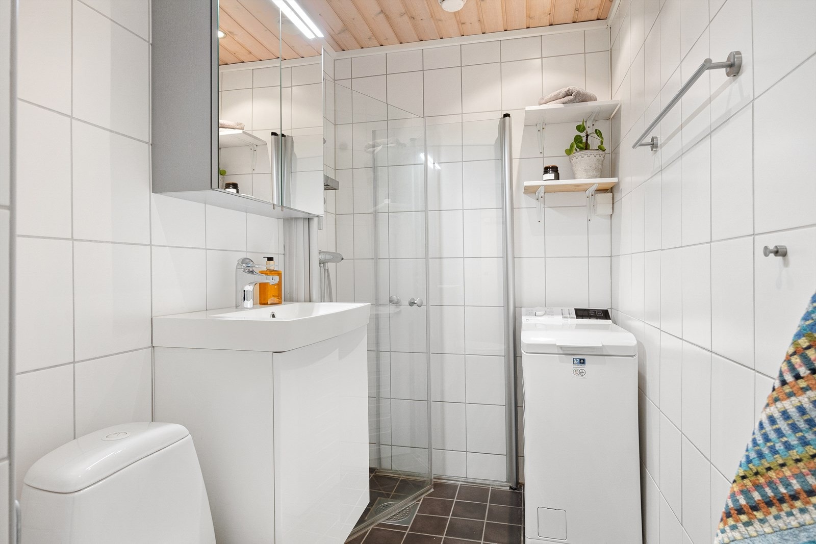 Badet har gulvstående toalett, dusjhjørne med vegg/dør i herdet glass, servant, skap, speil og belysning. Det er varmekabler i gulvet på badet og naturlig ventilasjon. Galleribilde