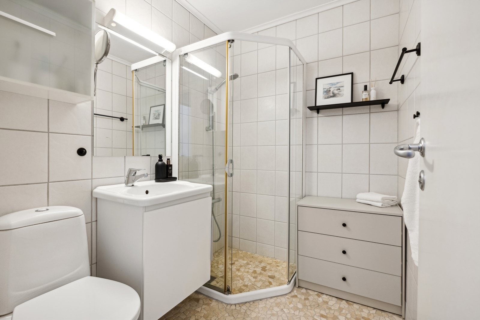 Badet er innredet med servant på skap, toalett, og dusj med glassdører. Galleribilde