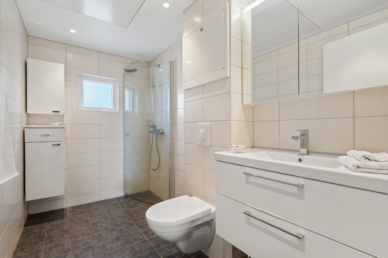 - Badet er innredet med benkeskap med servant, dusjdører i glass, vegghengt toalett og fordelerskap til "rør i rør" vannforsyning - Galleribilde