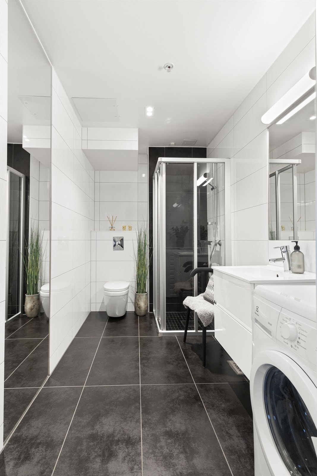 Badet er innredet med vegghengt skap med ovenpåliggende servant, speil med lys over, vegghengt toalett, samt dusjhjørne med skyvedører i glass. Nedfelt himling med downlights. Galleribilde