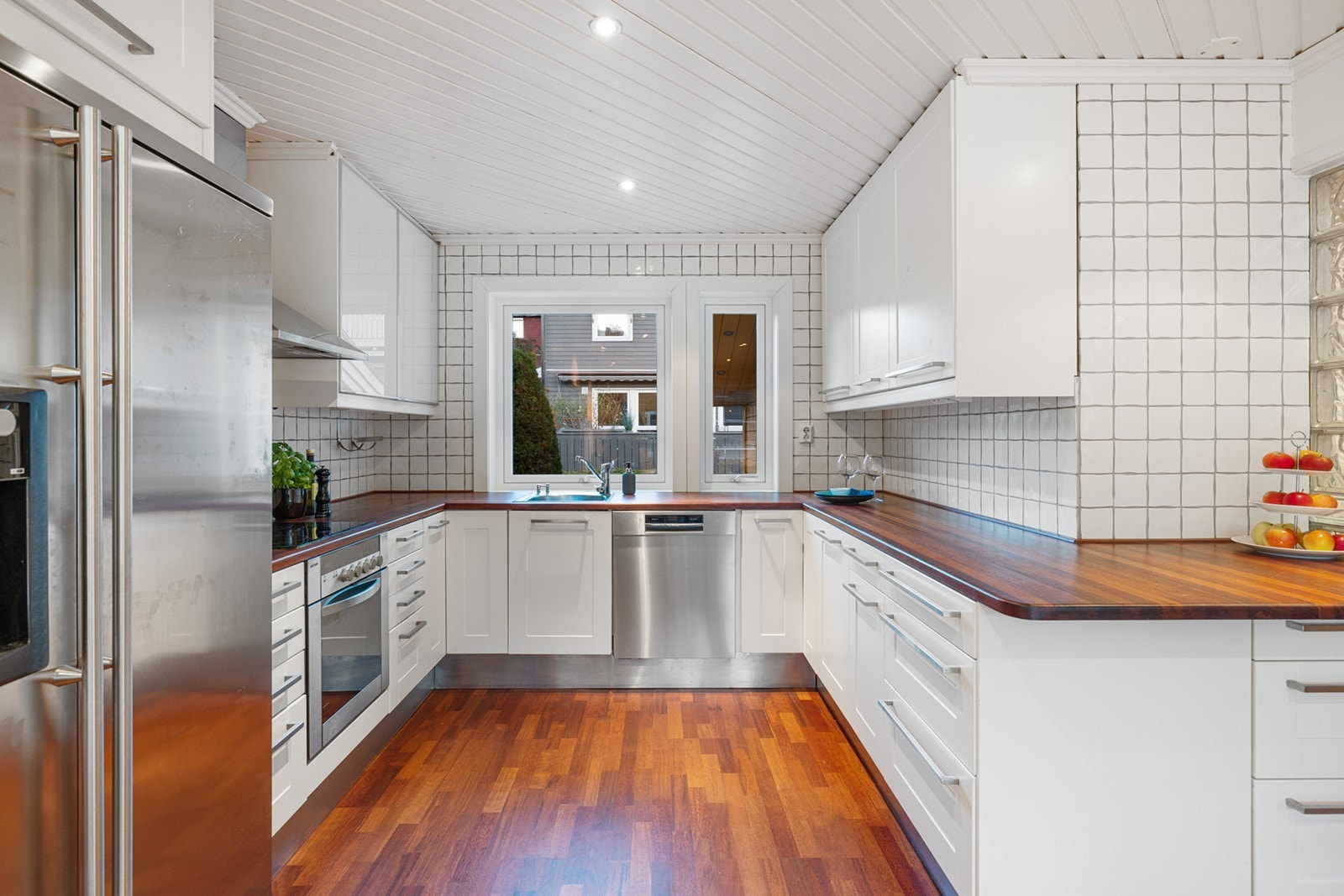 Kjøkkeninnredningen har hvite fronter med heltre benkeplate med nedfelt oppvaskkum med ett-greps blandebatteri, samt fliser mellom over og underskap. Galleribilde