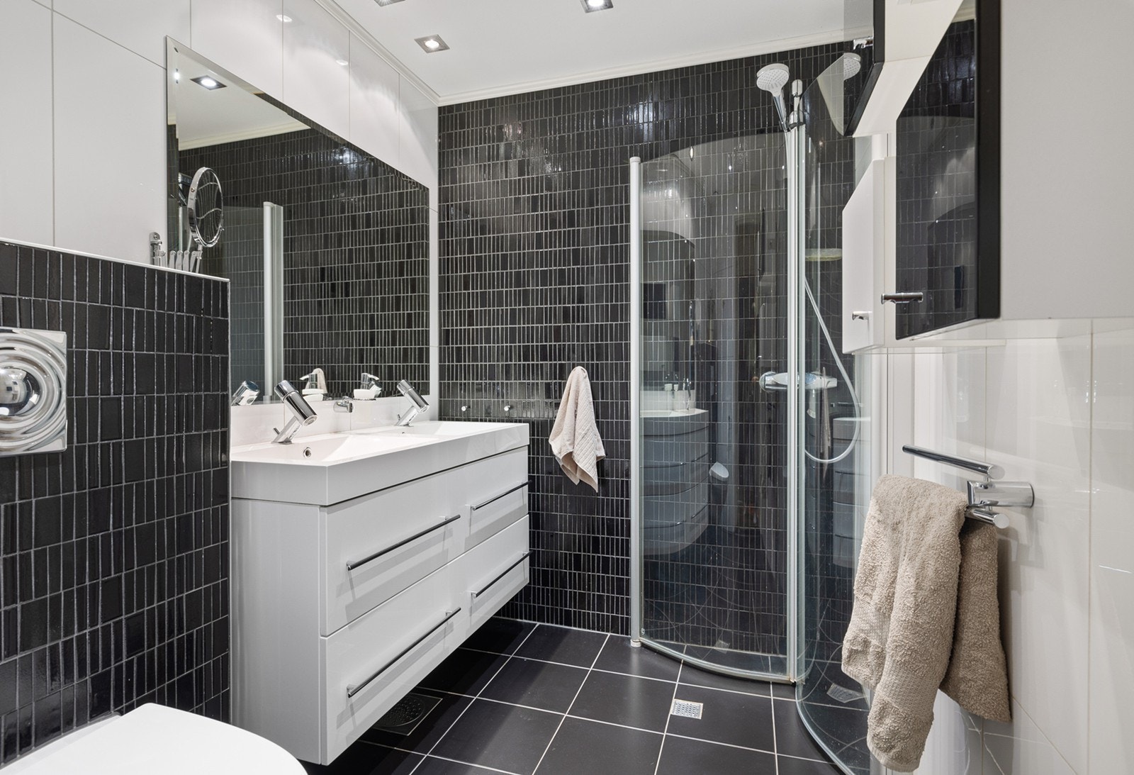 Badet er lekkert med hvite og sorte veggfliser, og sorte fliser på gulvet. Badet har downlights og gulvvarme. Et dusjhjørne med innfellbare glassvegger. Den øvrige innredningen består av dobbel servant med skuffer under og et stort speil med lys. Galleribilde