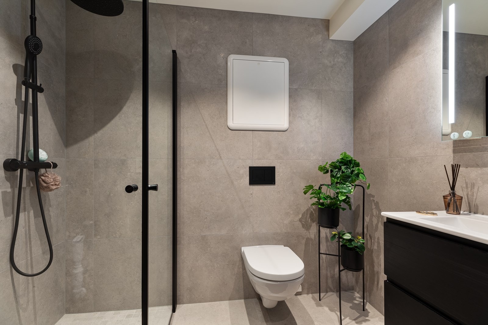 Lekkert bad i hybelen med vegghengt toalett, innredning, speil med belysning og dusj med dusjvegger i herdet glass. Galleribilde