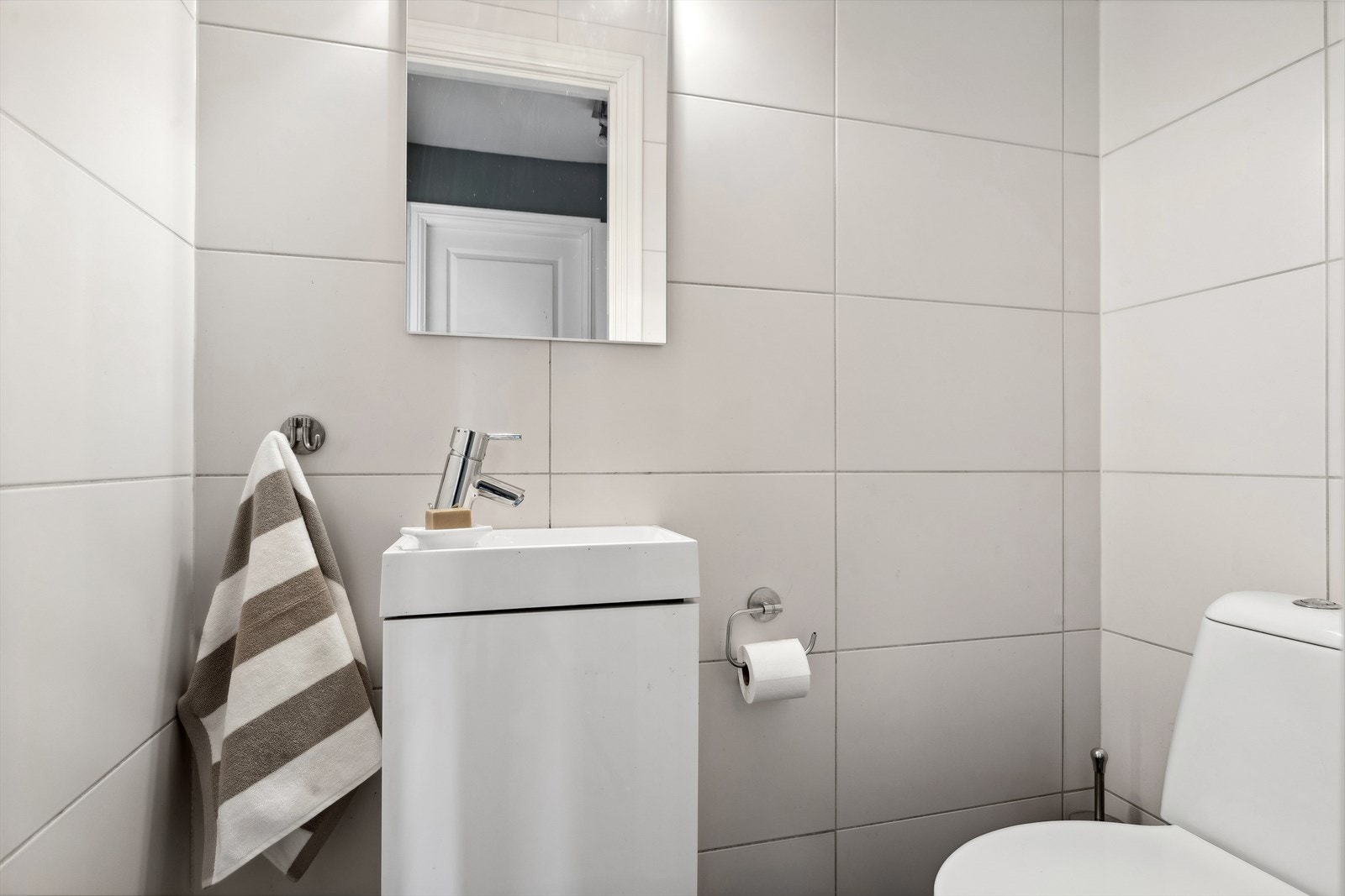 Toalettrom med fliser på gulv og vegger. Malt betong i himling. Gulvstående toalett. Innredning med nedfelt servant. Sentralt avtrekk i vegg. Galleribilde