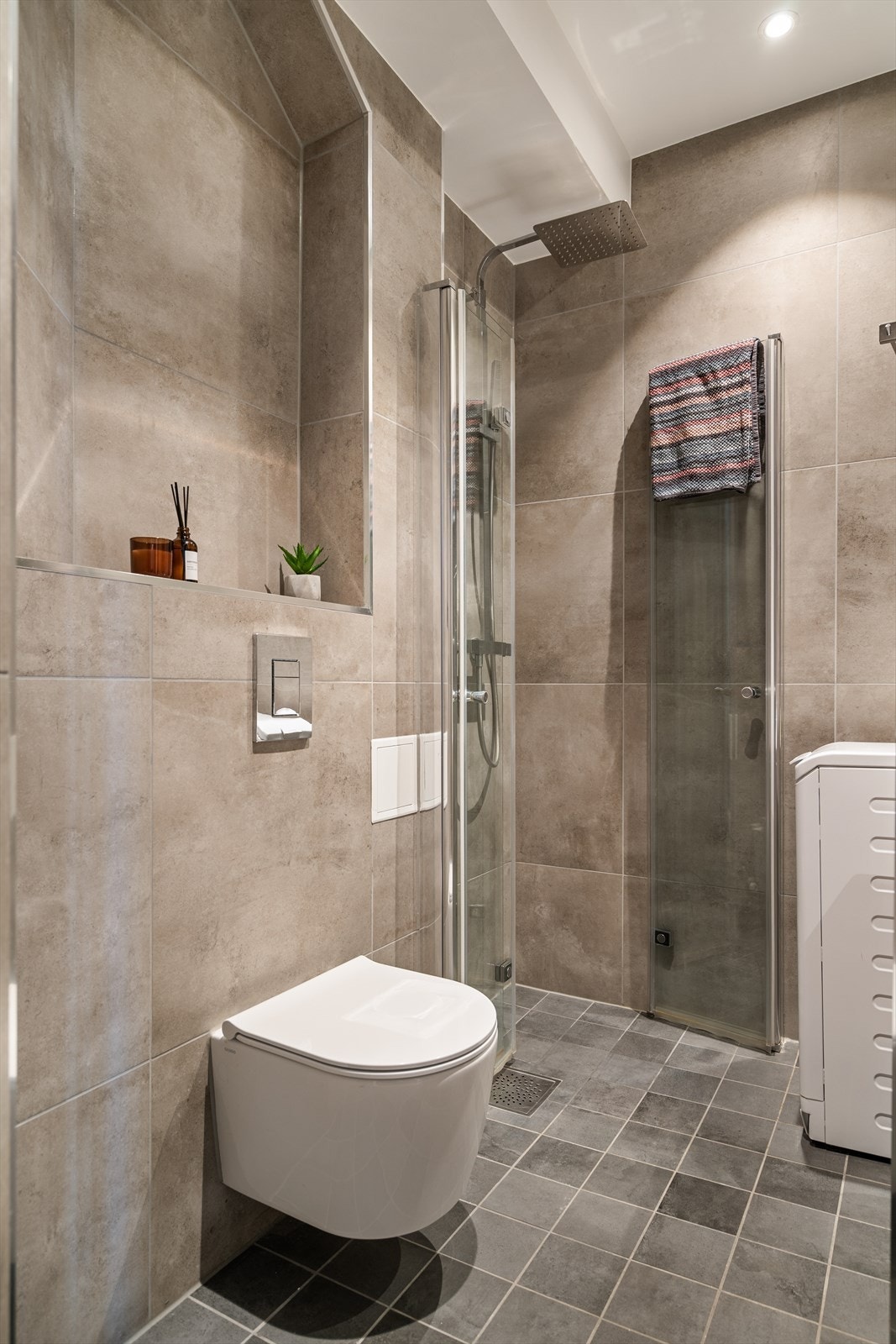 Rommet er innredet med blant annet vegghengt toalett og dusjhjørne med glassdører og regndusj. Legg merke til den flotte, flislagte nisjehyllen for ekstra oppbevaring. Galleribilde