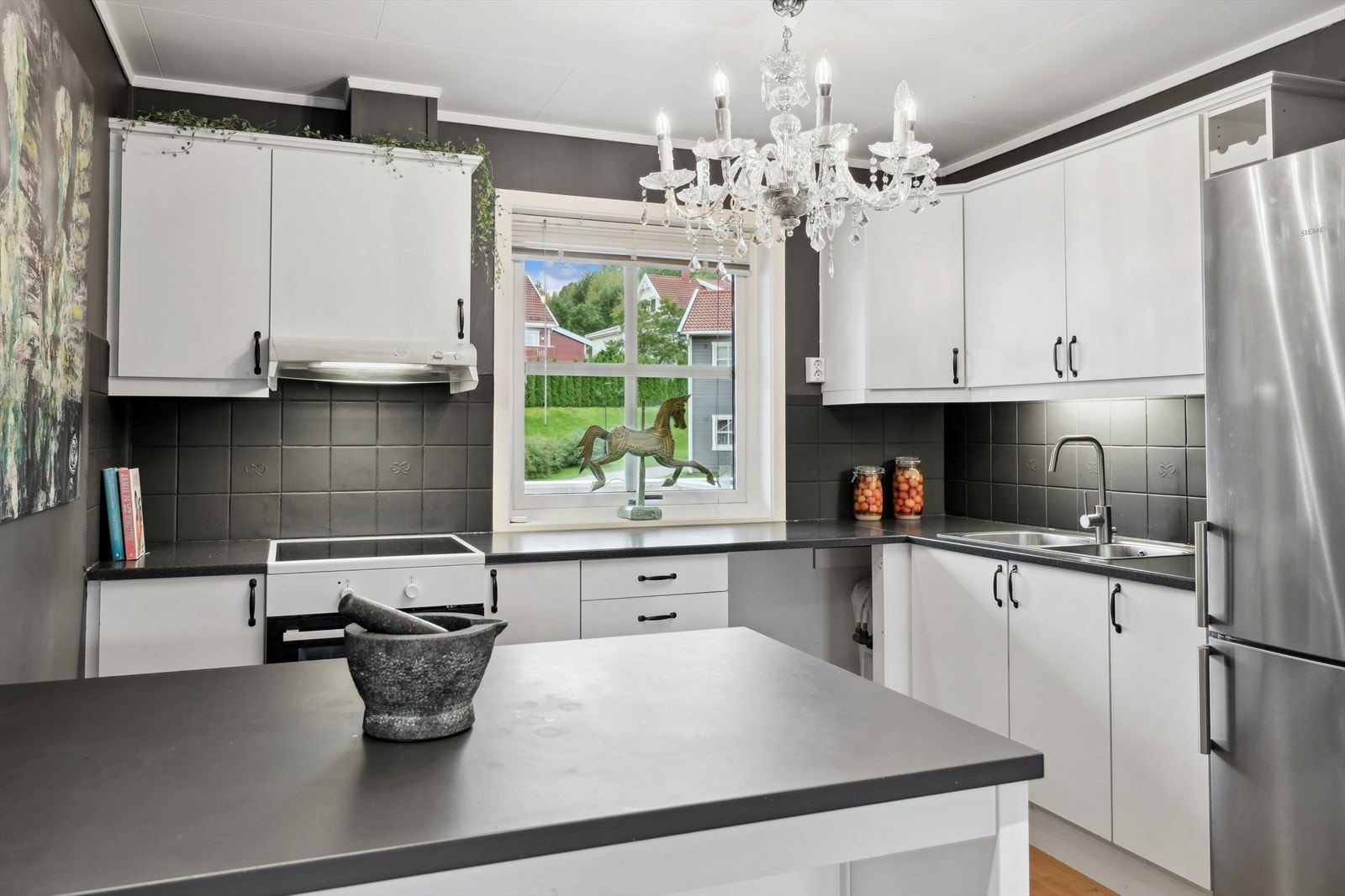 Lys kjøkkeninnredning med glatte fronter, benkeplater i laminat, fliser over benk, oppvaskkum med ett-greps blandebatteri og ventilator over kokesonen Galleribilde