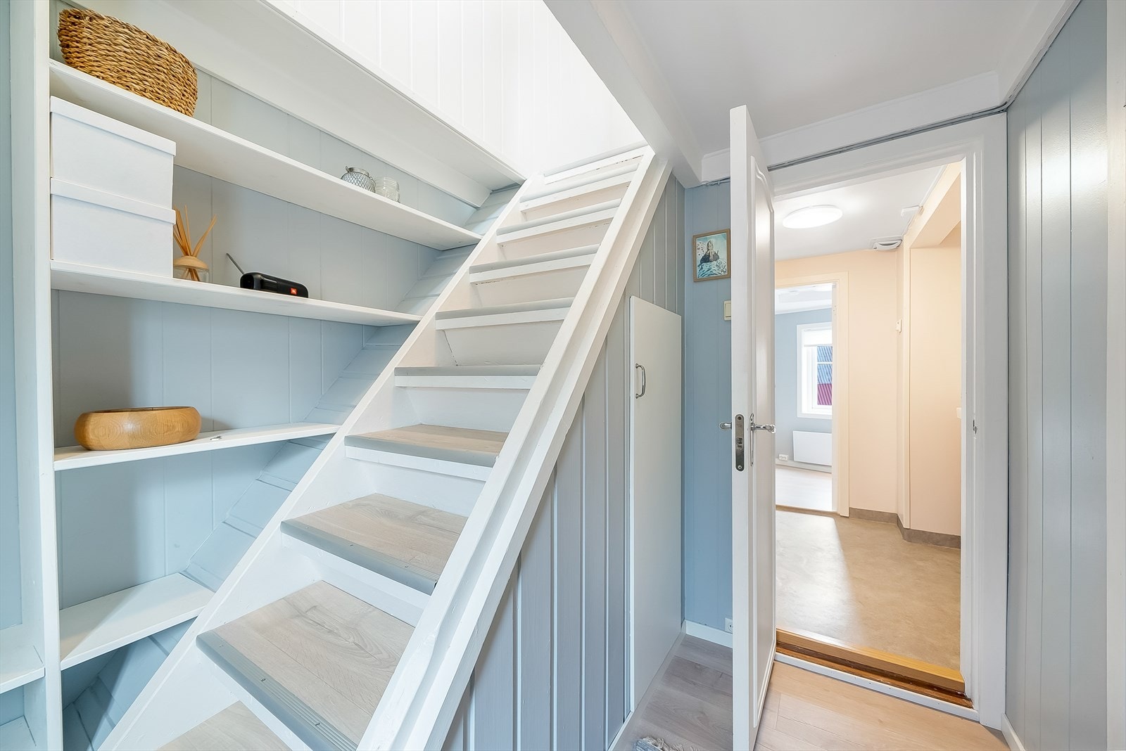 Trapp opp fra gangen til stua med praktisk hylleoppbevaring og bod under trappa. Galleribilde
