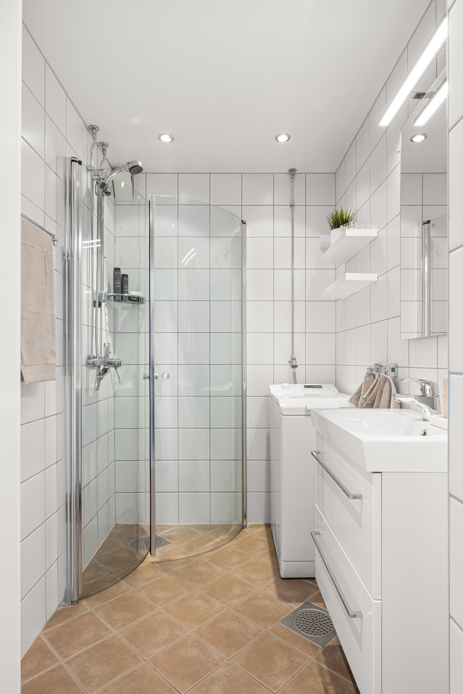 Badet har en hvit servantinnredning med skuffer, vegghengt speil med lys og dusjhjørne med innfellbare glassdører. Galleribilde