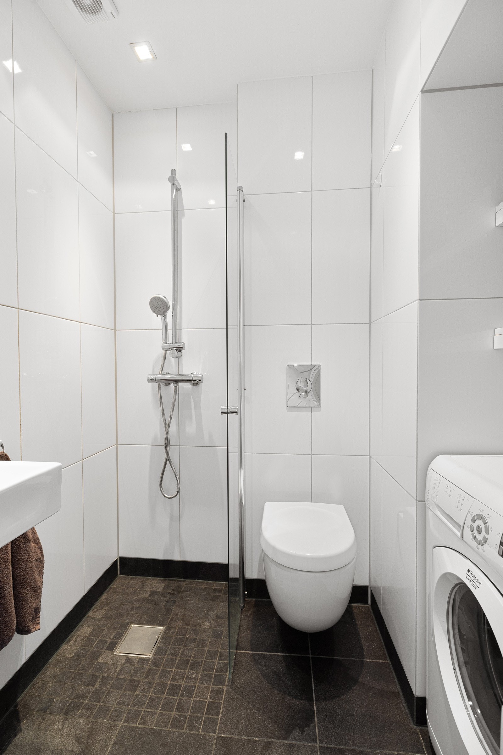 Flislagt bad med varmekabler, dusj, veggmontert servant og toalett samt opplegg for vaskemaskin Galleribilde
