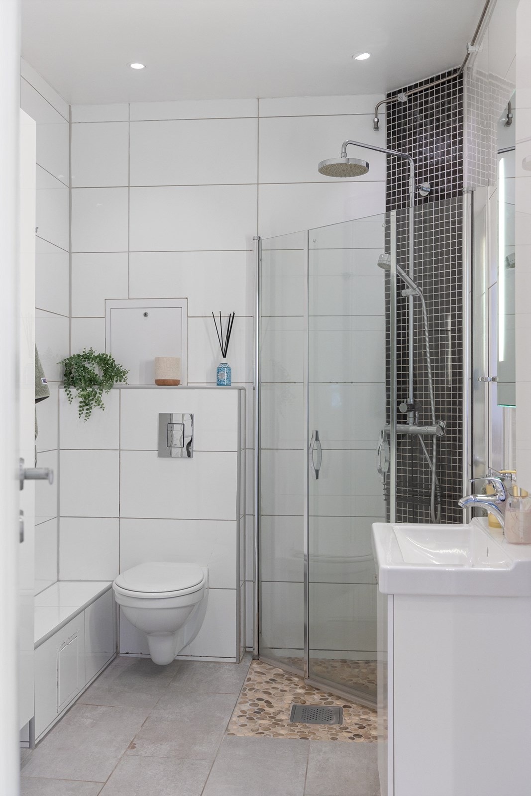 Badet inneholder baderomsinnredning med skap, servant og speil, veggmontert toalett og dusjhjørne Galleribilde