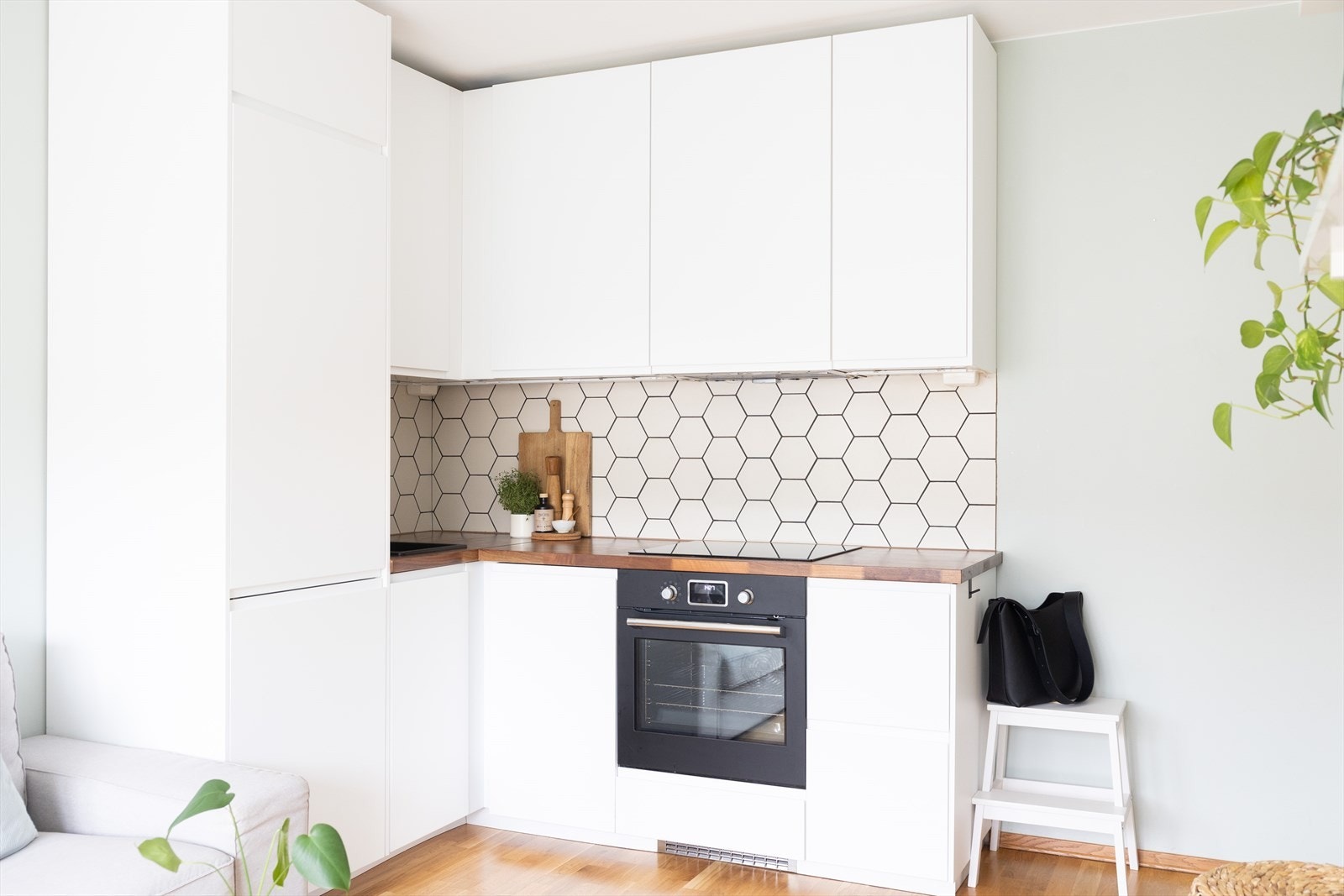 Kjøkkeninnredning med hvite, slette fronter og benkeplate av heltre. Mellom over- og underskap er det lekre heksagon fliser Galleribilde