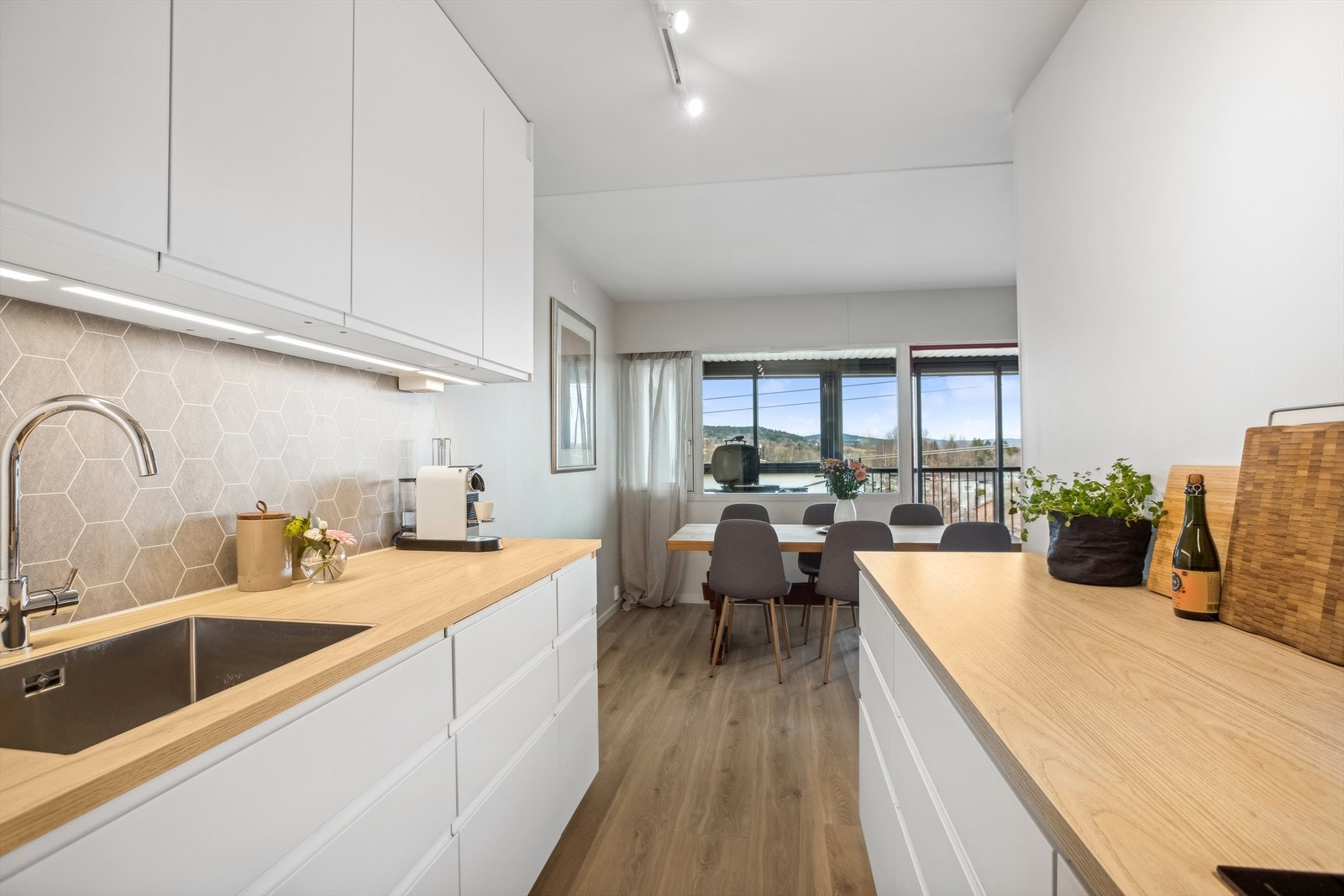 Benke- og overskap med slette fronter, benkeplate av laminat, stålplate på vegg bak platetetopp og kitchenboard på vegg bak oppvaskkum. Galleribilde