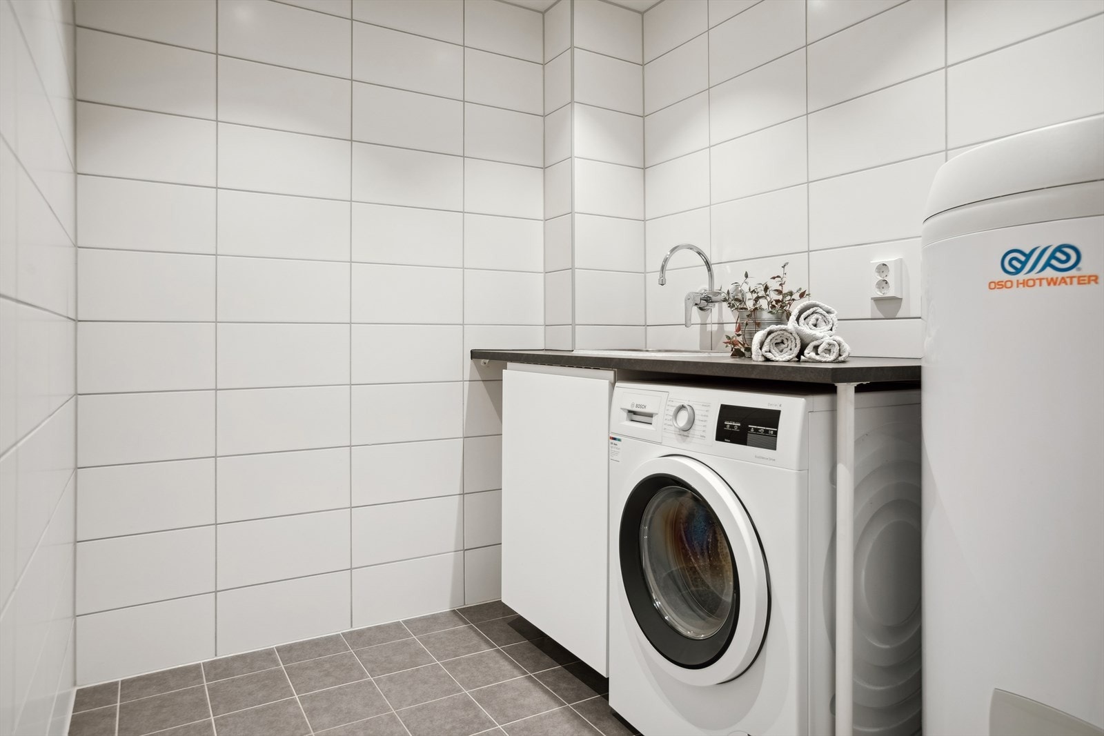 Vaskerom rehabilitert i regi av borettslaget i 2021. Flislagte vegger og himling med downlights. Innredning med slette fronter og benkeplate av laminat med nedsenket utslagsvask med 1-greps blandebatteri og avløpsrør av plast. Opplegg for vaskemaskin. Galleribilde