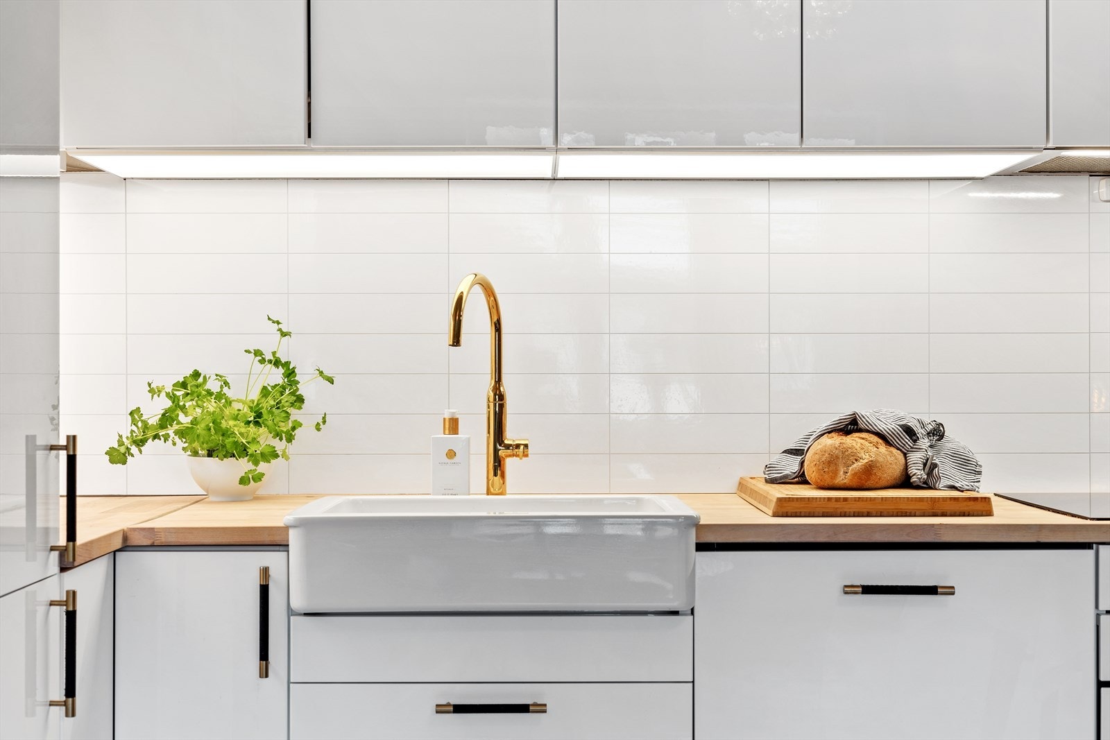Benkeplate i tre. Oppvaskkum i porselen med ett-greps armatur fra IKEA. Laminerte plater mellom benkeplate og overskap. Stikkontakt og overbelysning over benk. Galleribilde