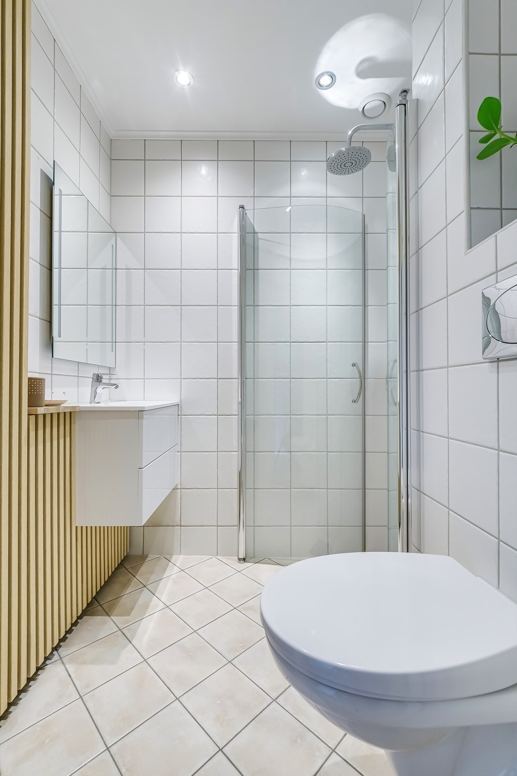 Badet er innredet med servant i skuffeseksjon for oppbevaring, vegghengt toalett og dusjhjørne med innfellbare glassdører Galleribilde