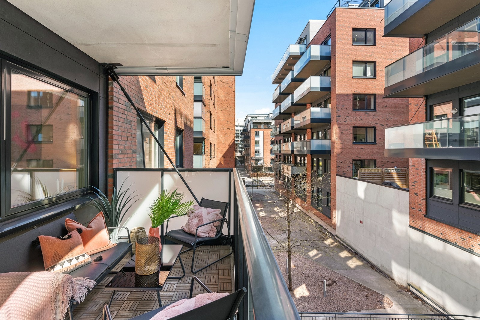 Overbygd balkong med god plass til utemøblement. Treheller på gulv, utebelysning på veggen og rekkverk i frostet glass. Galleribilde