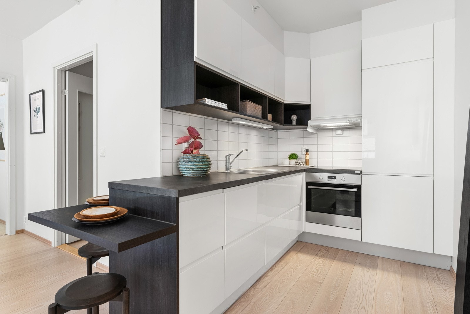 Innredningen har hvite høyglansfronter med gripekant og dempefunksjon, samt mørk benkeplate i laminat med trestruktur og nedfelt vaskekum i stål. Galleribilde