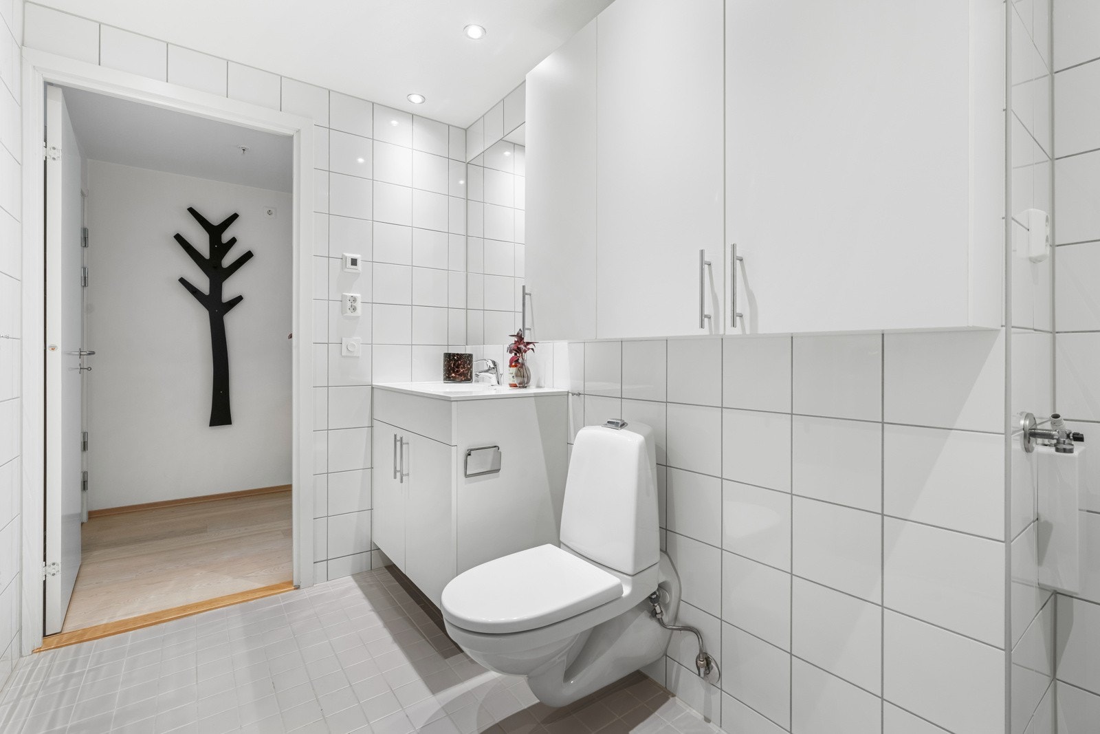 Innredningen består av en heldekkende servant på hvitt skap, stort servantspeil, hvite veggskap og et veggmontert toalett. Galleribilde