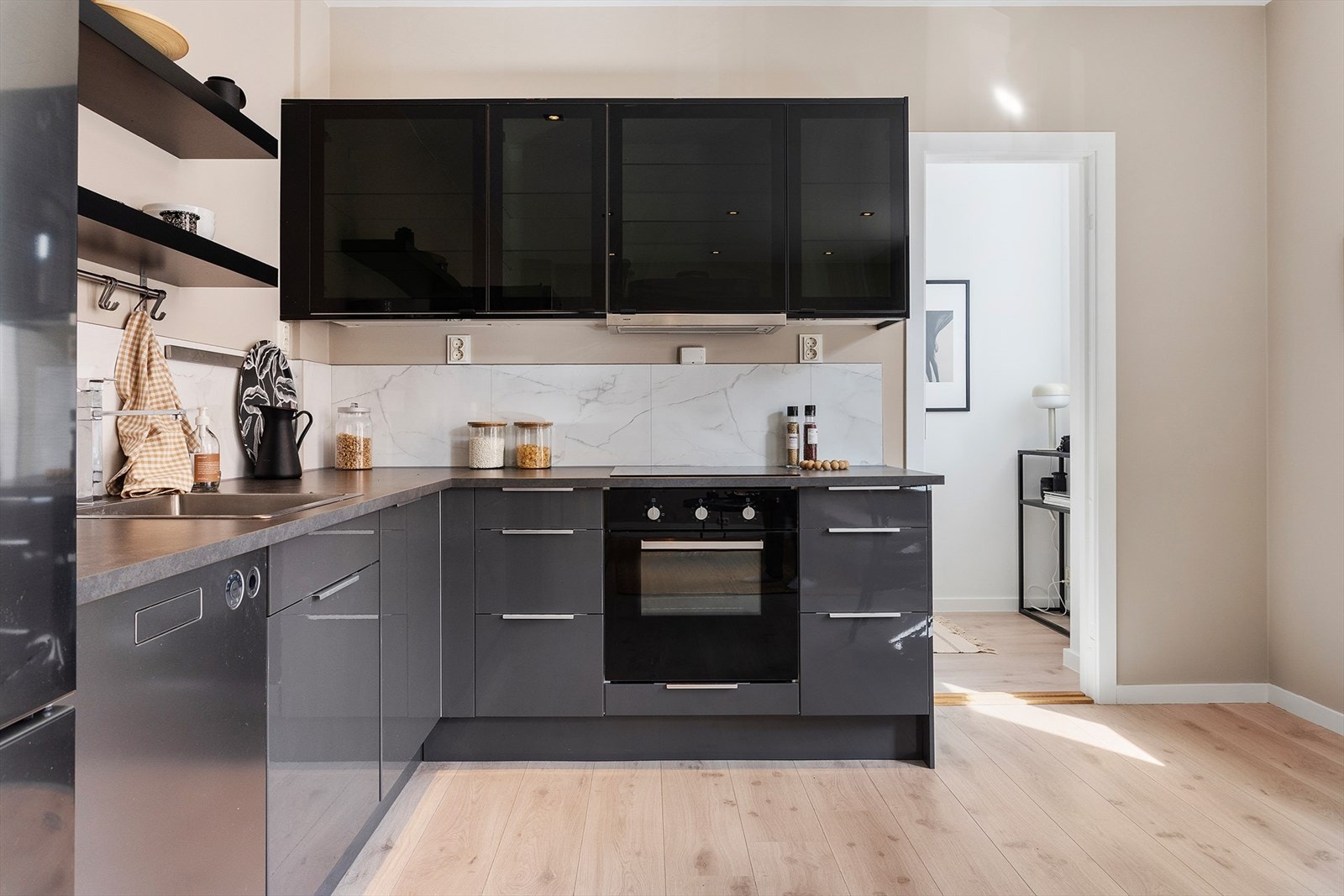 Stilrent kjøkken med sorte fronter, plater mellom overskap og laminert benkeplate. Galleribilde