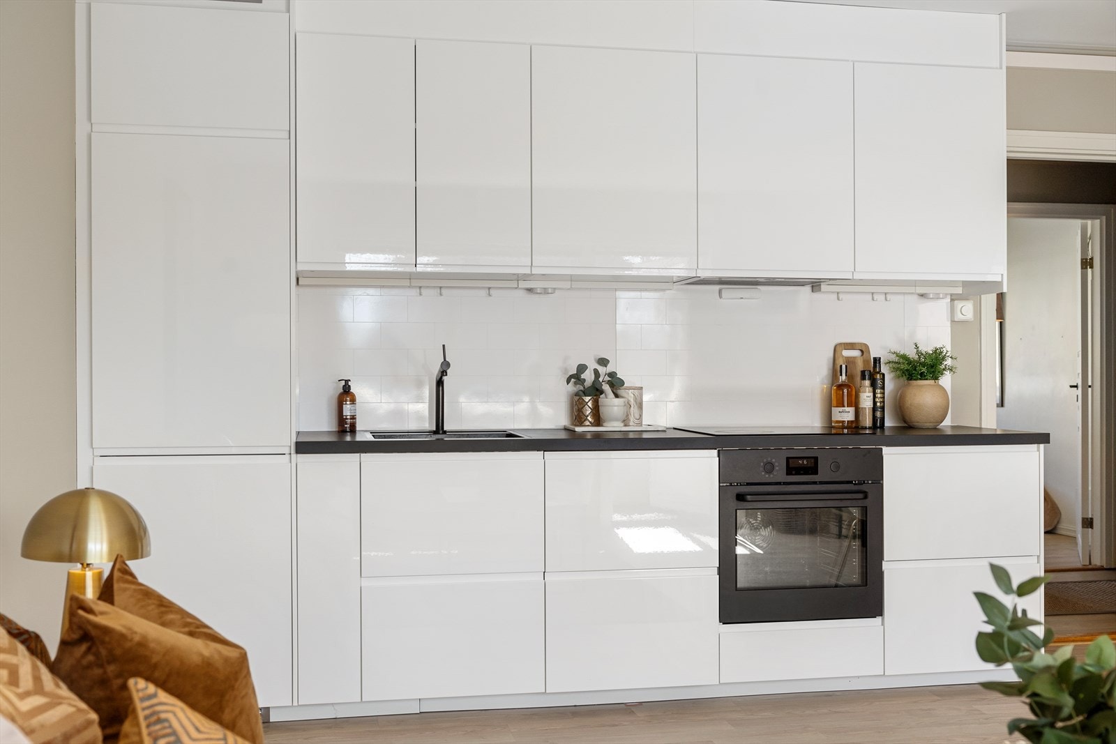 Stilrent IKEA-kjøkken fra 2019 med god skap- og benkeplass. Kjøkkenet har høyglansfronter, laminatbenkeplate med kum, flisliknende plater på vegg over benken og lys under overskapene. Galleribilde