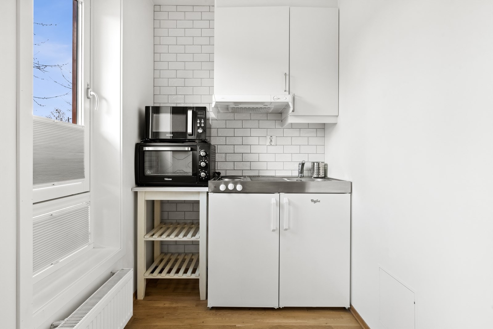 Hybeldel: Kjøkkeninnredningen har hvite slette fronter og benkeplate av stål. I innredningen er det montert kjøleskap og platetopp Galleribilde