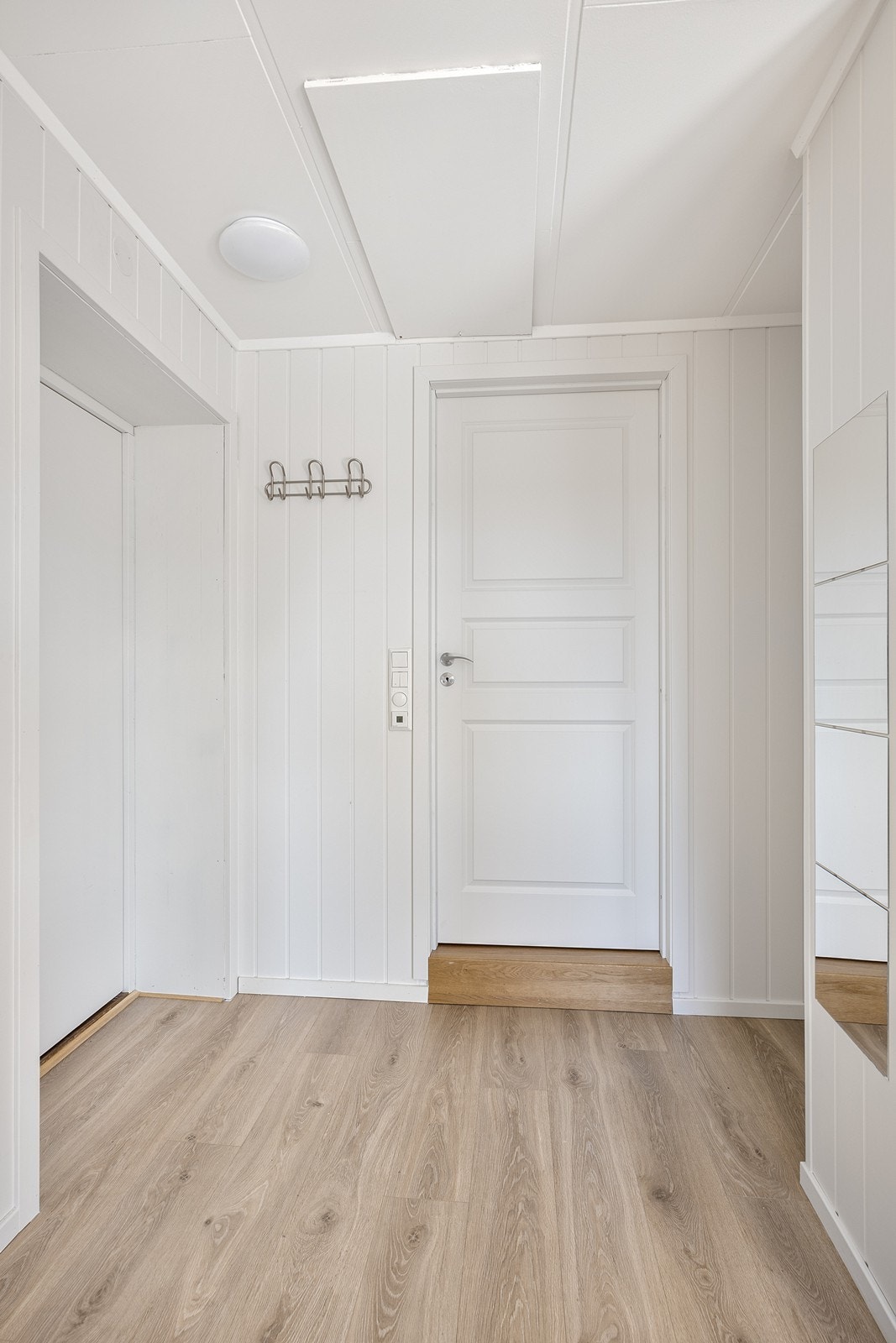 Entreen har laminatgulv og lysmalt veggpanel, noe som gir et representativt inntrykk av hva som venter lengre inn Galleribilde
