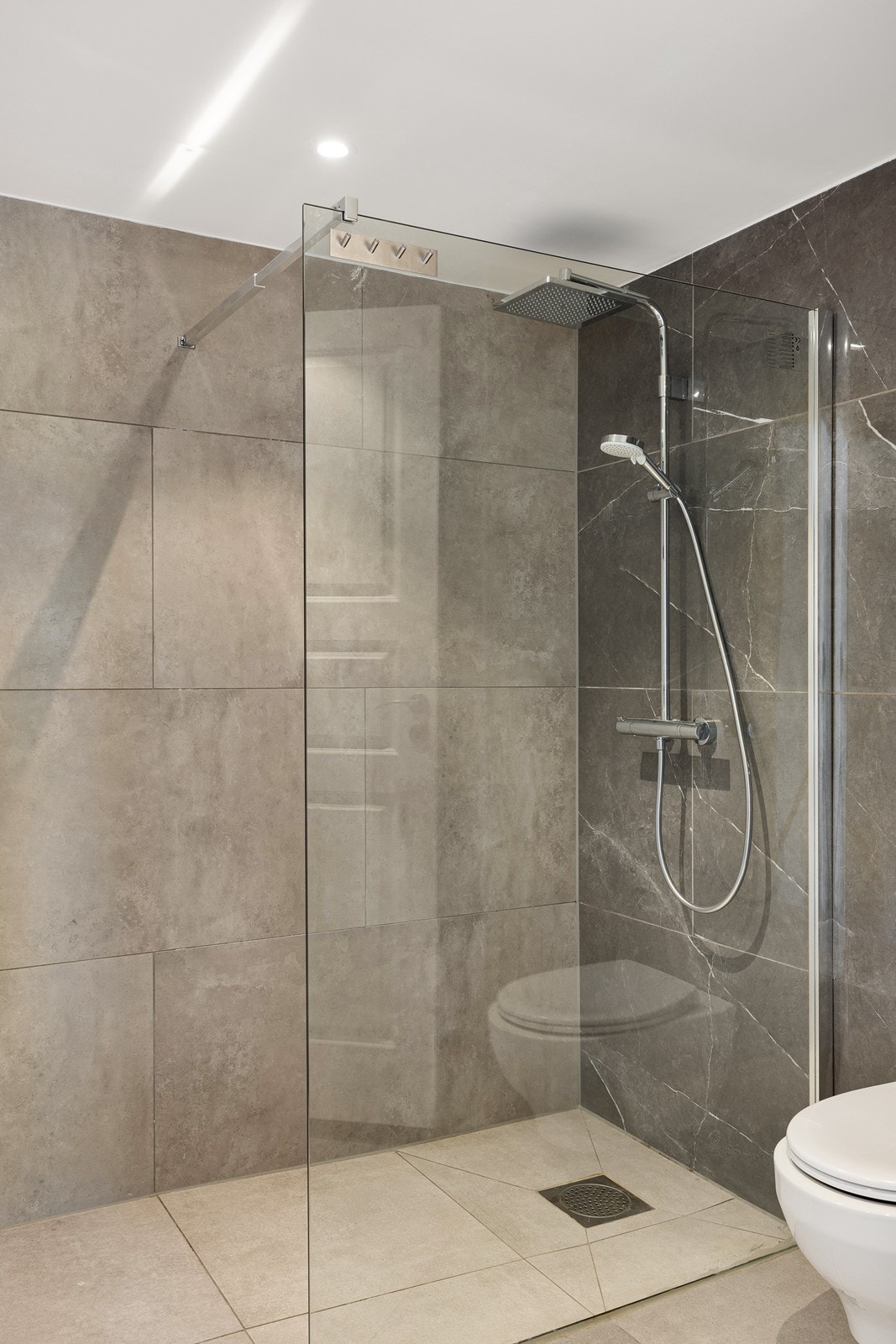 Badet har veggmontert toalett og et dusjhjørne med regnfallsdusj Galleribilde