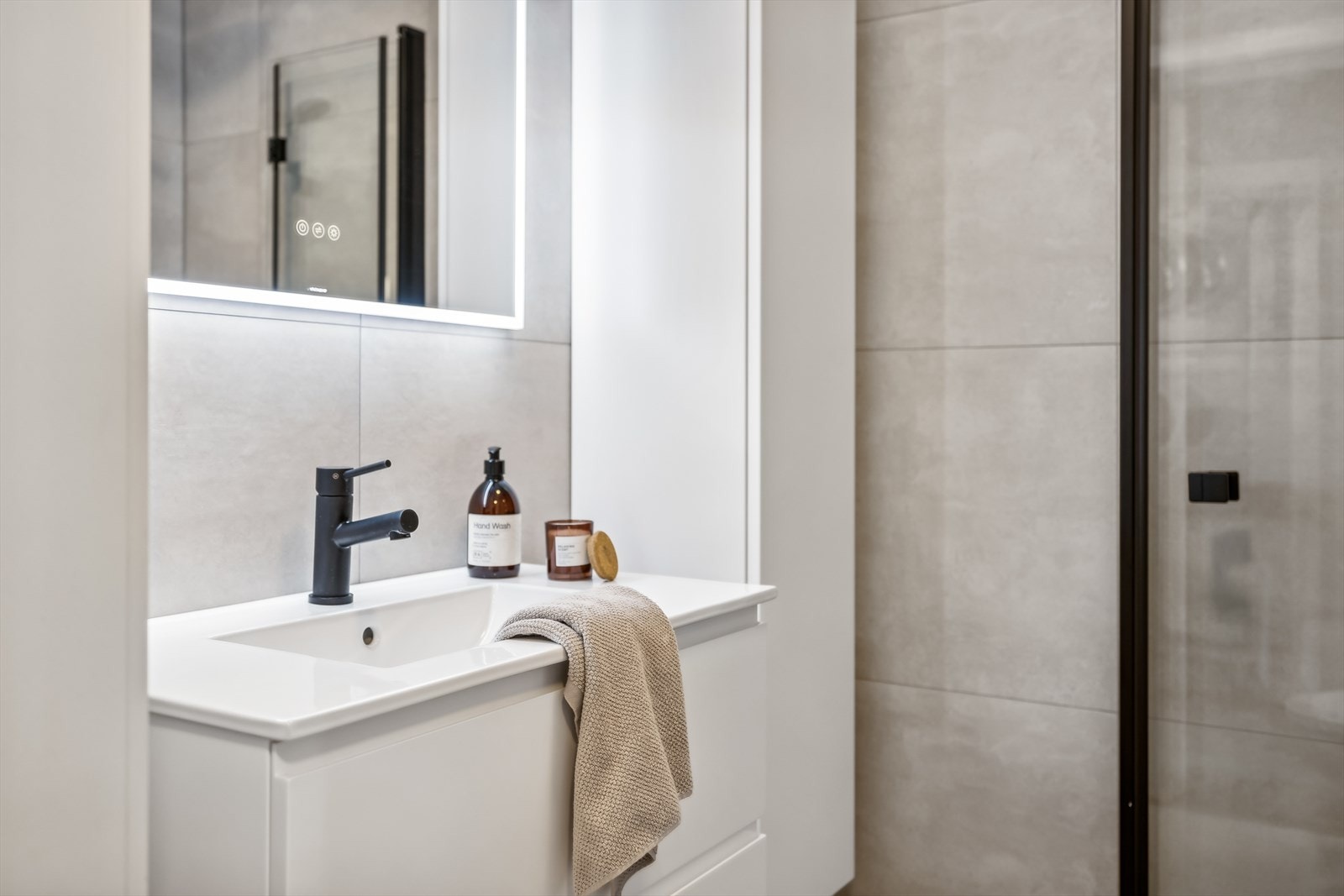 Badet er innredet med toalett, dusjhjørne med innfellbare glassdører og baderomsinnredning med nedfelt servant på skuffer. Galleribilde