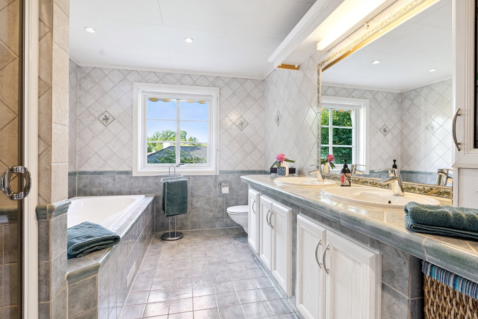 Flislagt baderom i 2. etasje med to nedfelte servanter, toalett, innfliset badekar og dusjvegger/ hjørne Galleribilde