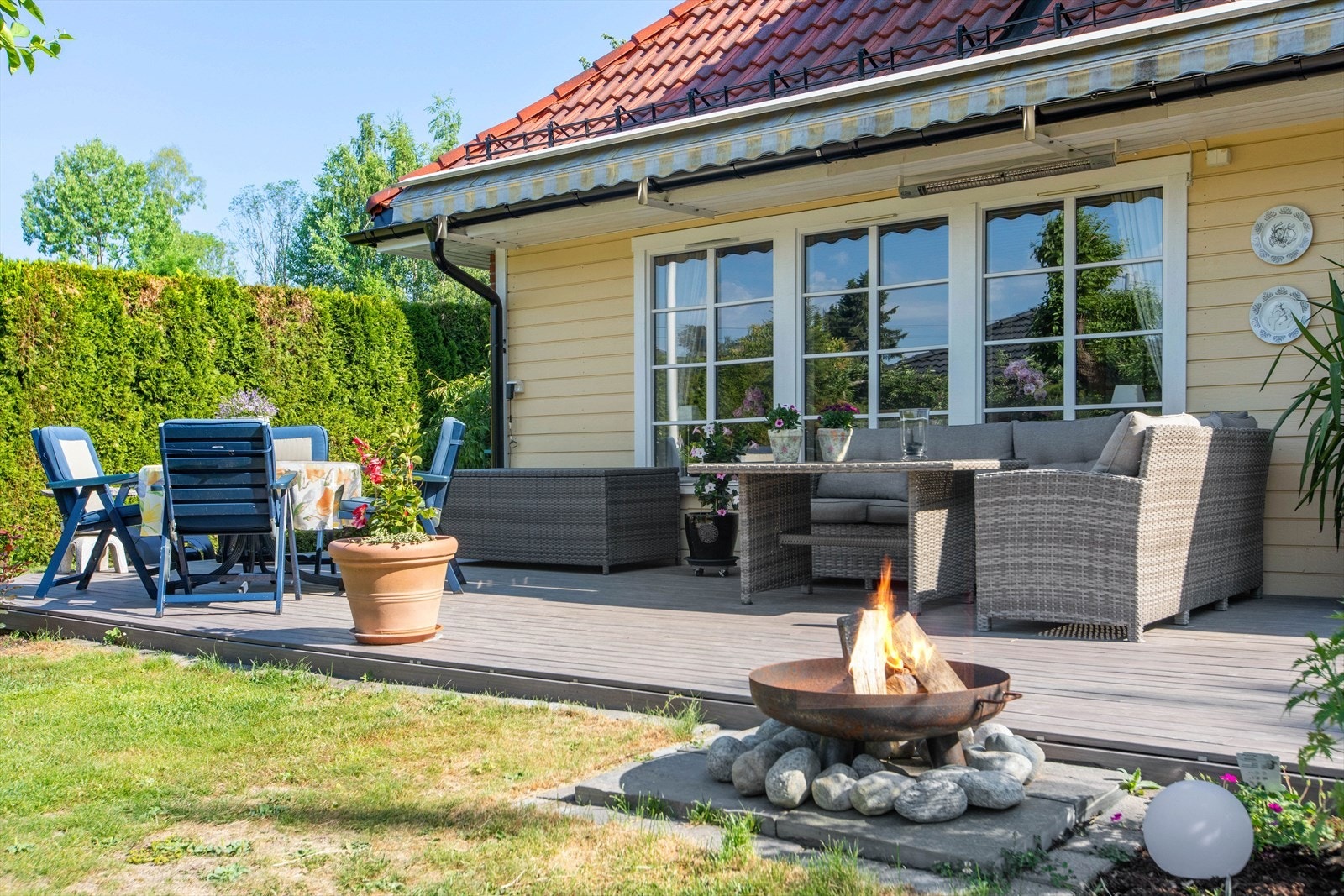 Stor og solrik terrasse med bålpanne. Hagen er pent opparbeidet med plen og diverse beplanting. Galleribilde