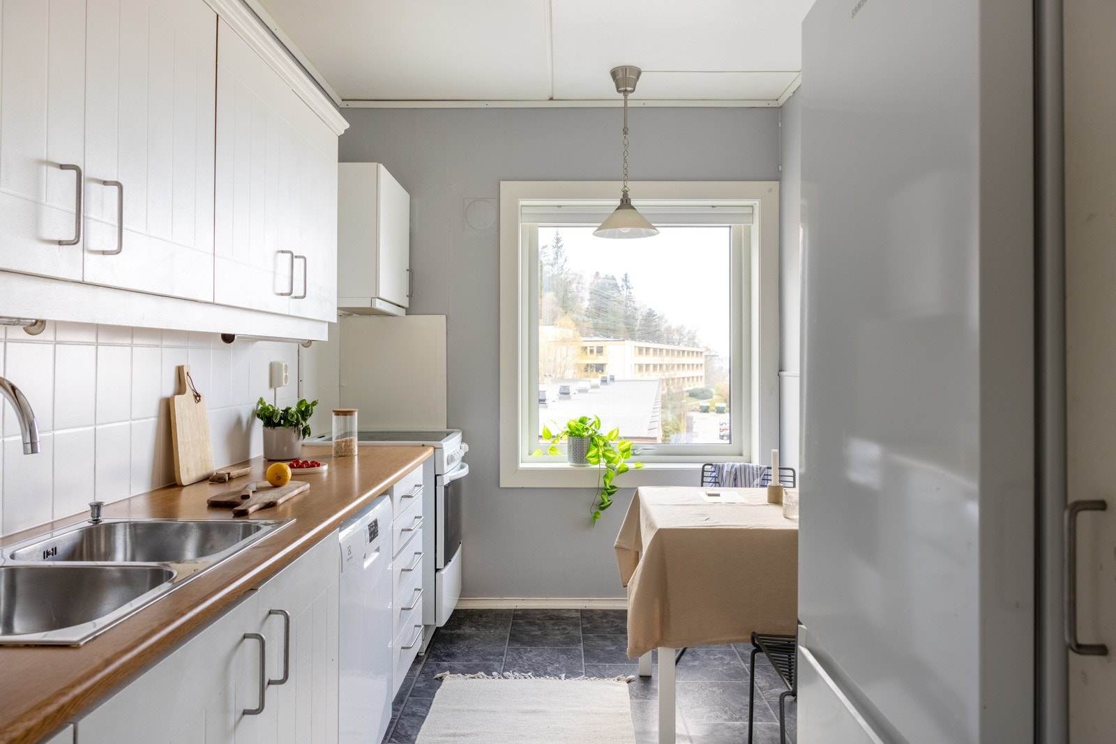 Romslig kjøkken med profilerte hvite fronter og laminat benkeplate med nedfelt vask av stål. Galleribilde