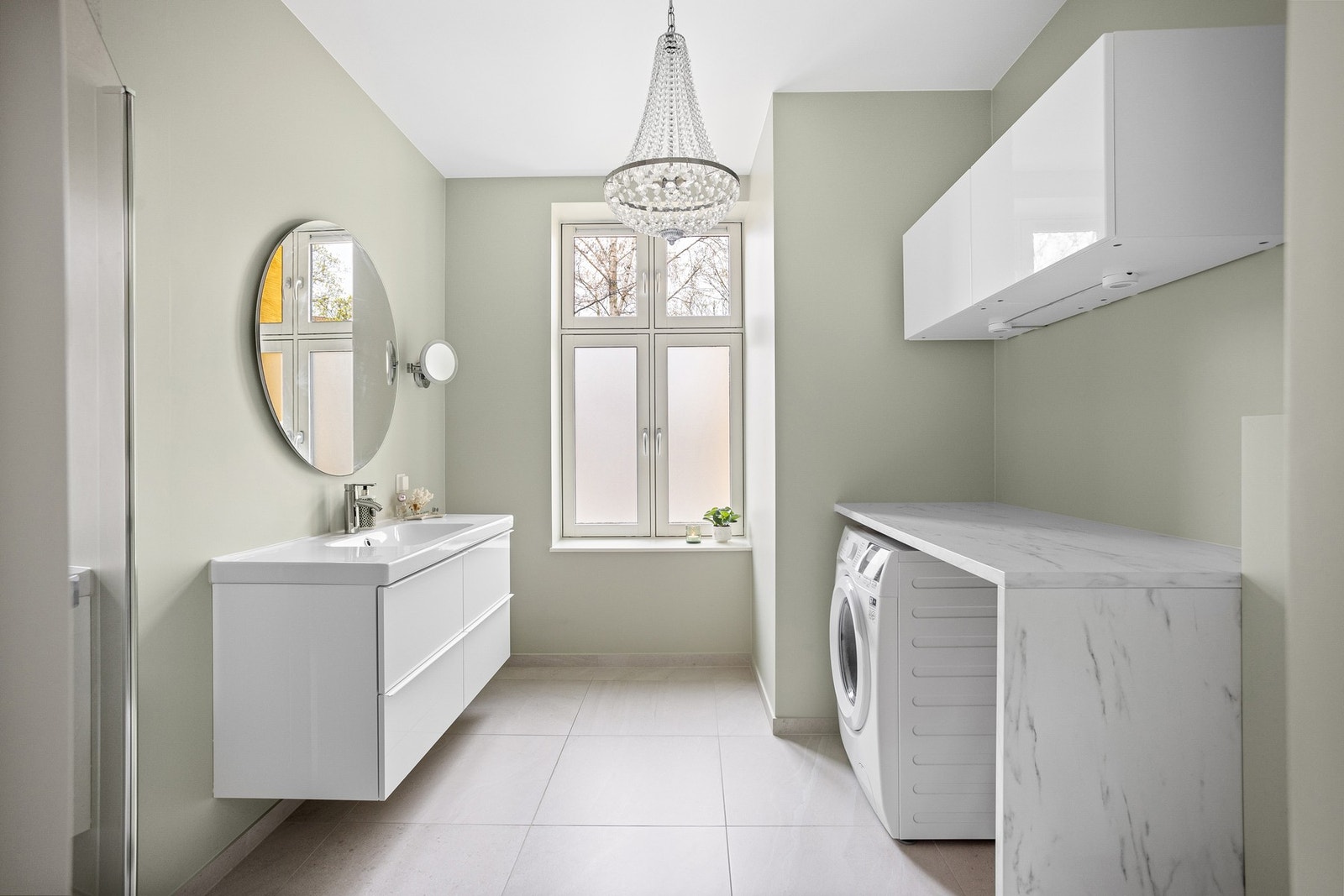 Baderommet har store lyse fliser på gulv med gulvvarme, glatte overflater malt i en fin farge og stor klassisk vindusflaste som slipper inn deilig dagslys. Galleribilde