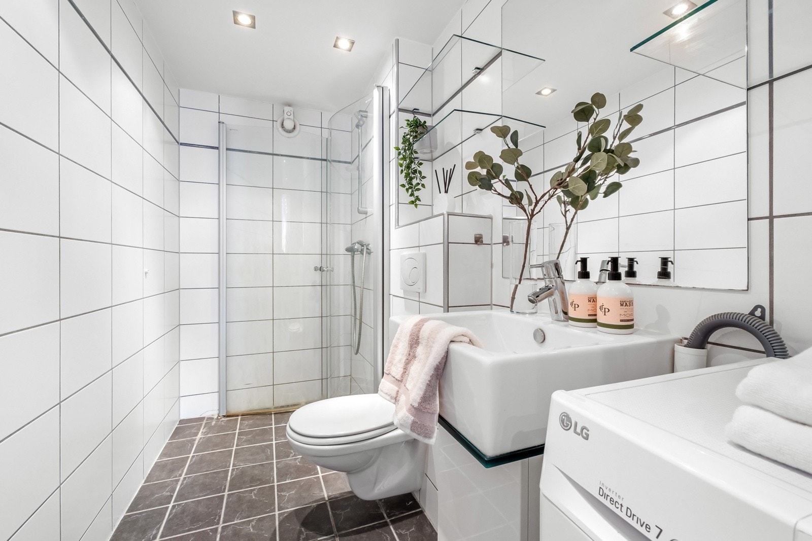 Romslig baderom med flislagte vegger, nedforet himling med downlights og heldekkende italiensk designvaskeservant med glassplater og veggspeil. Galleribilde
