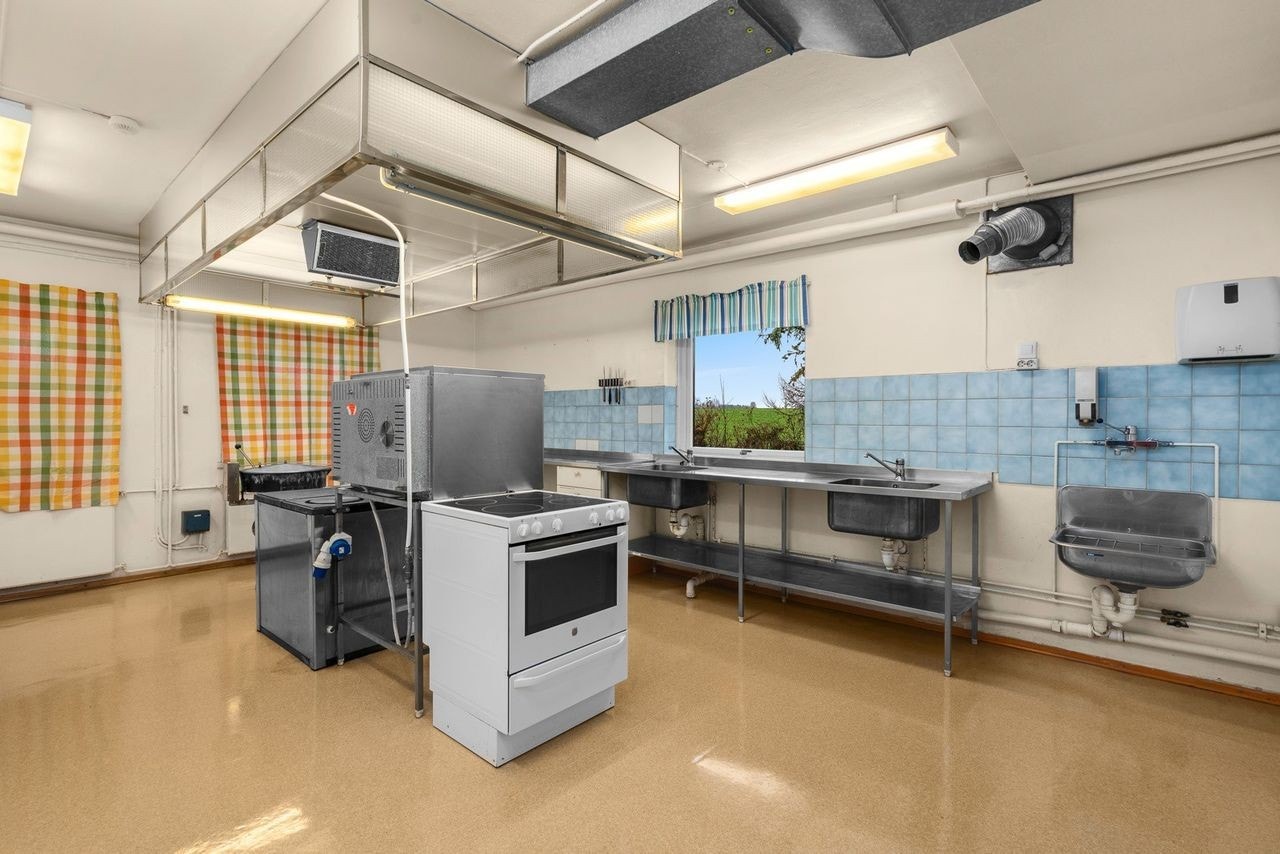 Industrikjøkken i underetasjen med hvite slette fronter og laminert benkeplate i kombinasjon med benkebeslag i rustfritt stål m/to kummer. Galleribilde